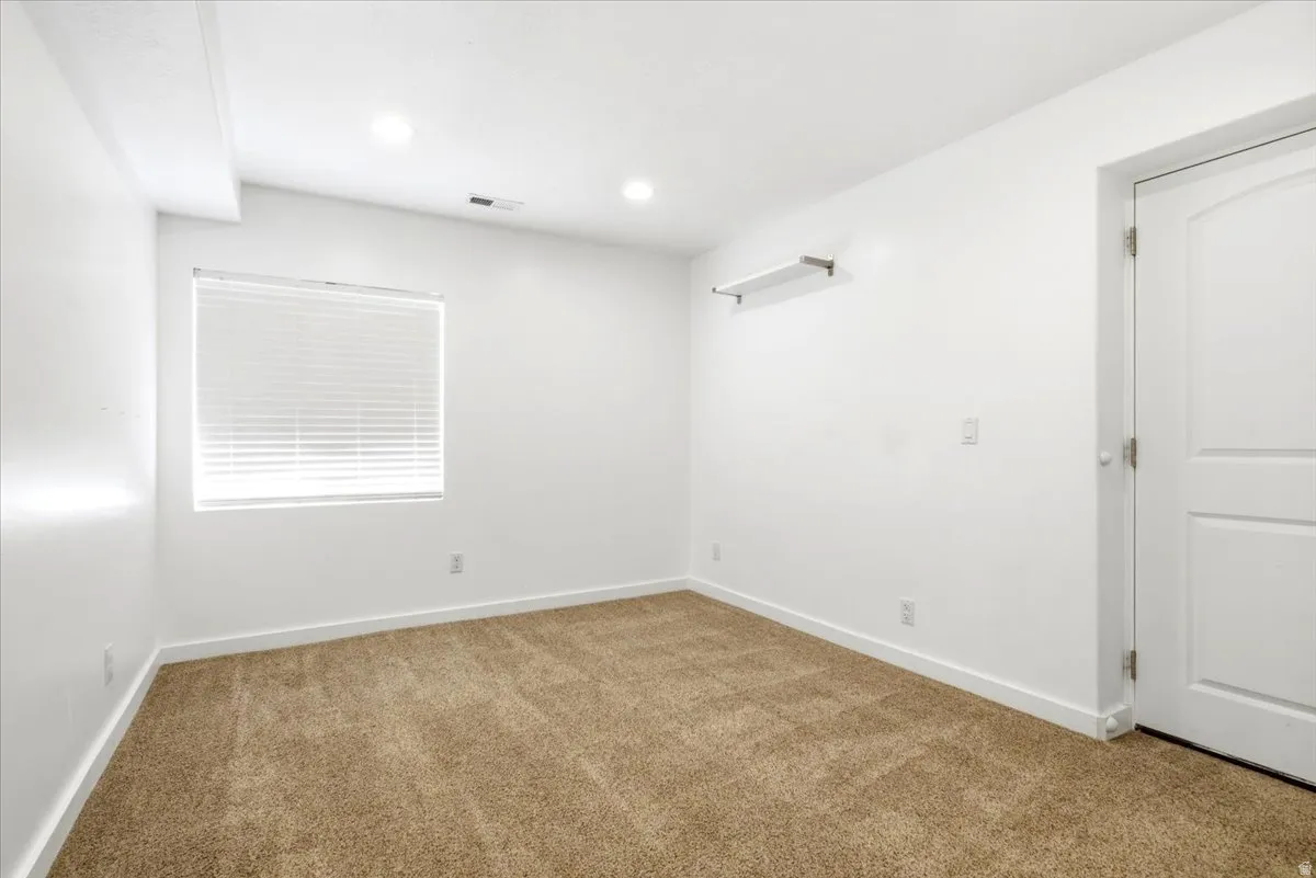 Spacious room featuring neutral carpeting, white walls, recessed lighting, and a window with blinds