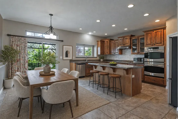 Kitchen and dining area featuring warm wood cabinetry, granite countertops, a tile backsplash, and stainless steel appliances including double wall ovens