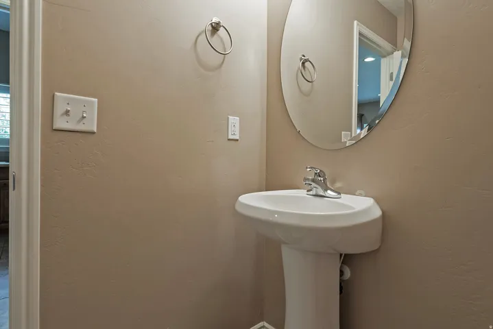 Pedestal sink with chrome faucet, complemented by a frameless oval mirror and a chrome towel ring