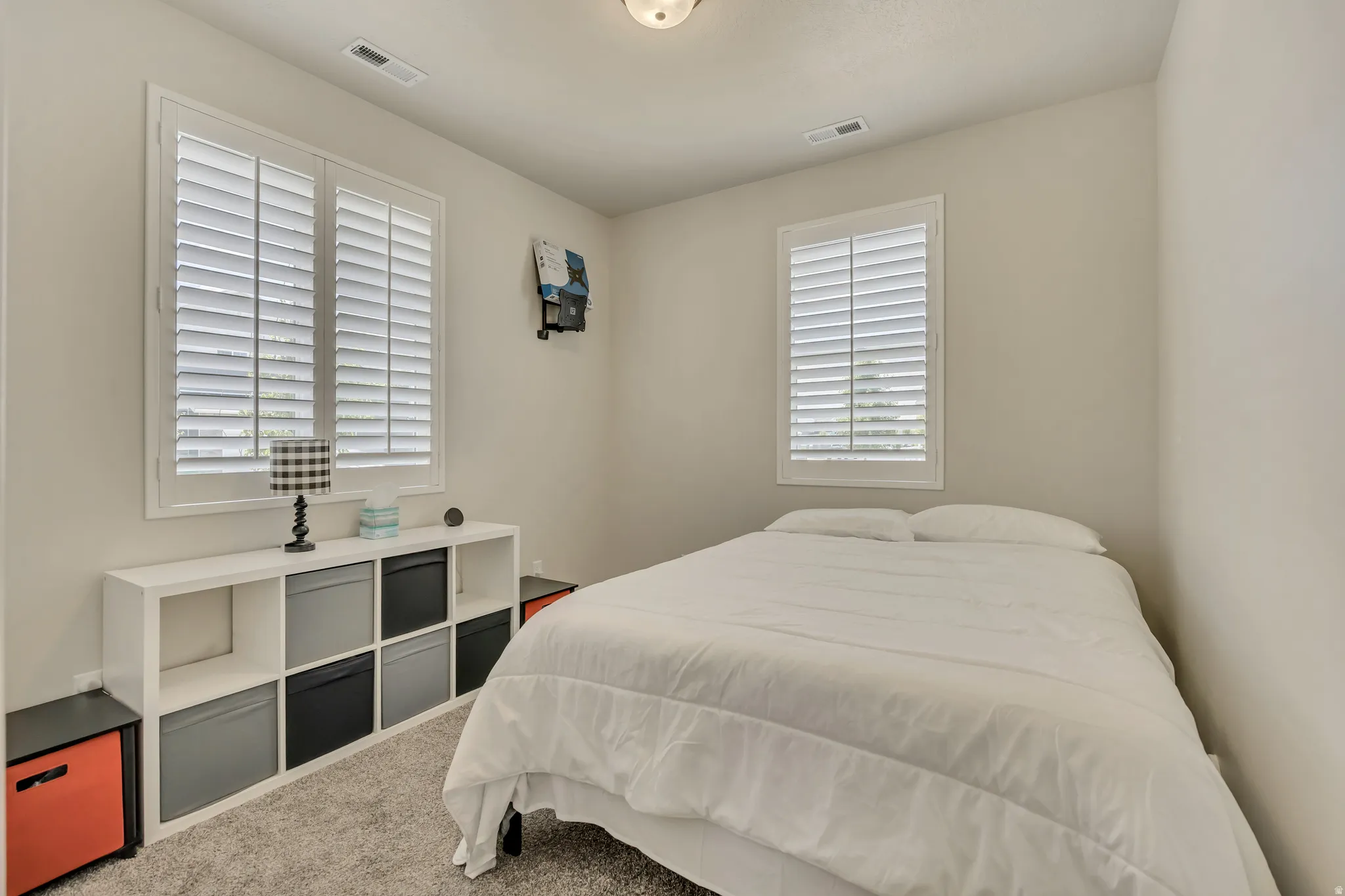 Carpeted room featuring two windows with white plantation shutters, neutral wall paint, and a ceiling-mounted light fixture