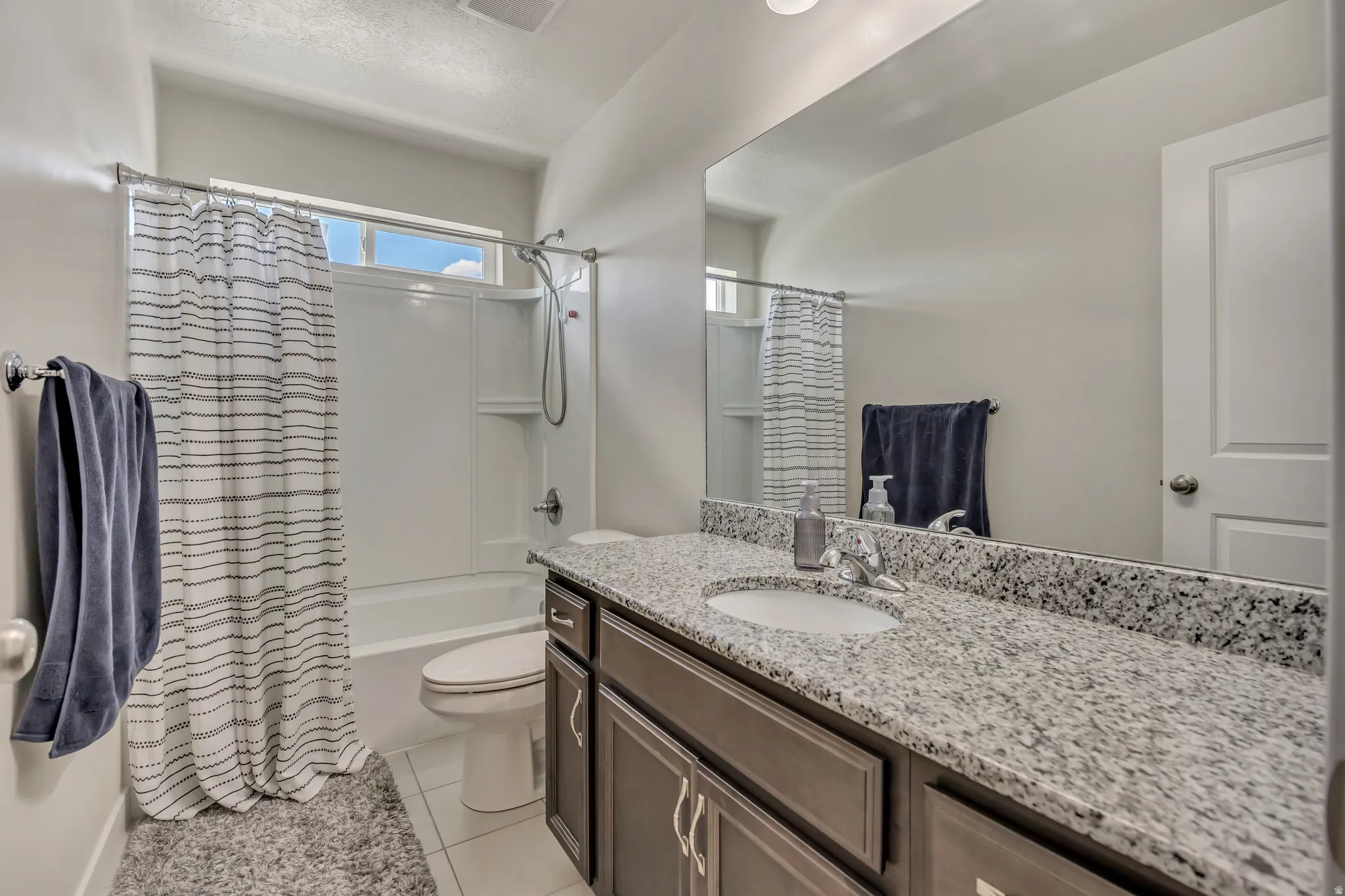 Bathroom featuring a white tub-shower combination with an overhead window, a single vanity with stone-finish countertop, and integrated sink