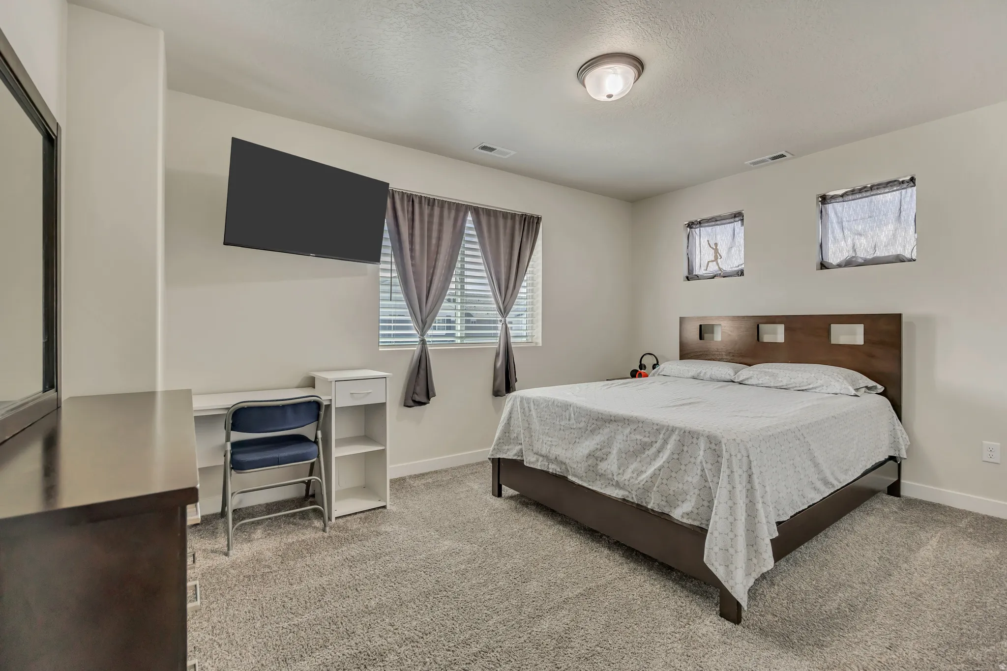 Carpeted room featuring multiple windows with blinds, a ceiling-mounted light fixture, and a wall-mounted television