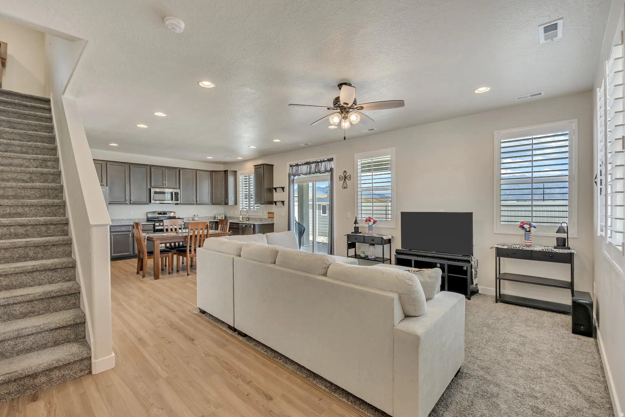 Open-concept living space featuring wood-finish flooring, recessed lighting, a ceiling fan, and plantation shutters