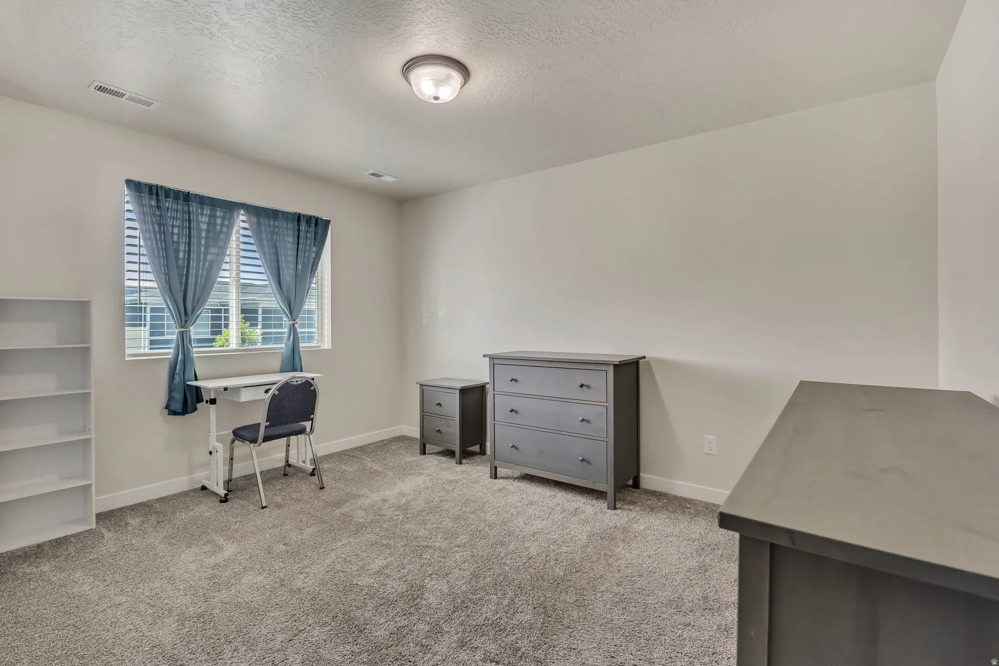 Carpeted room with a ceiling light fixture, white walls, and a window featuring blinds