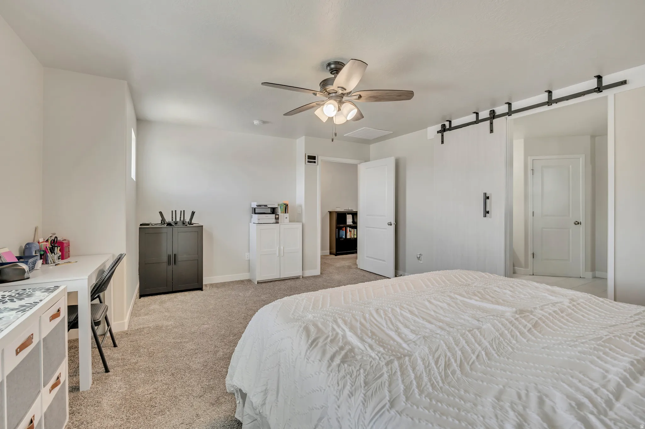 Carpeted room featuring a ceiling fan with light fixture, a window providing natural light, and a modern barn door on a black metal track
