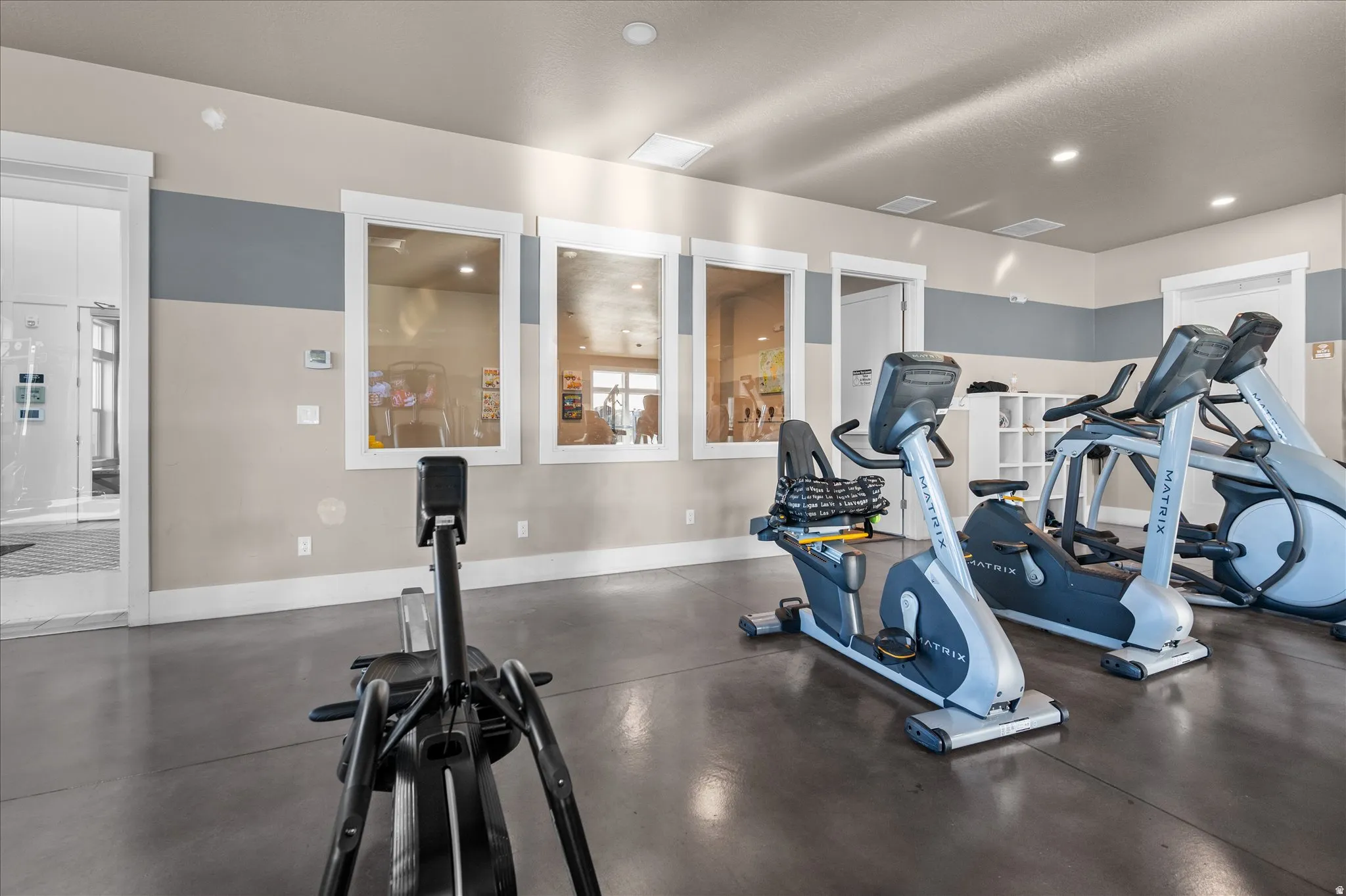 Recreational fitness area featuring smooth concrete flooring, a neutral two-tone painted wall, and multiple bright recessed ceiling lights