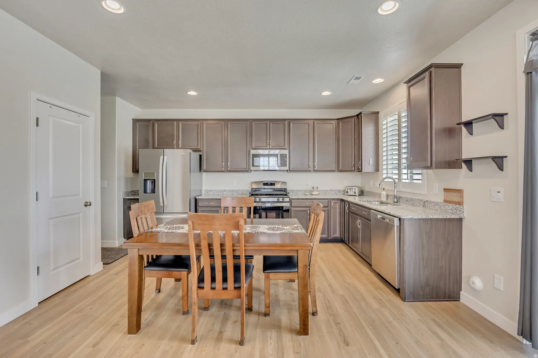 Open-concept kitchen featuring wood-finish flooring, recessed lighting, and dark wood cabinetry with stainless steel appliances