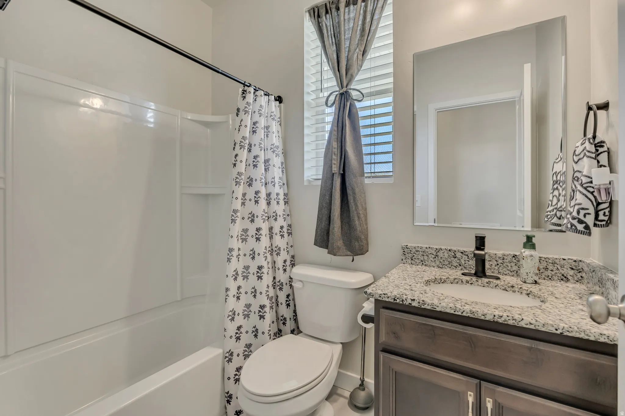 Bathroom featuring a white tub/shower combination, dark wood-finish vanity with a granite-style countertop, undermount sink, and matte black faucet