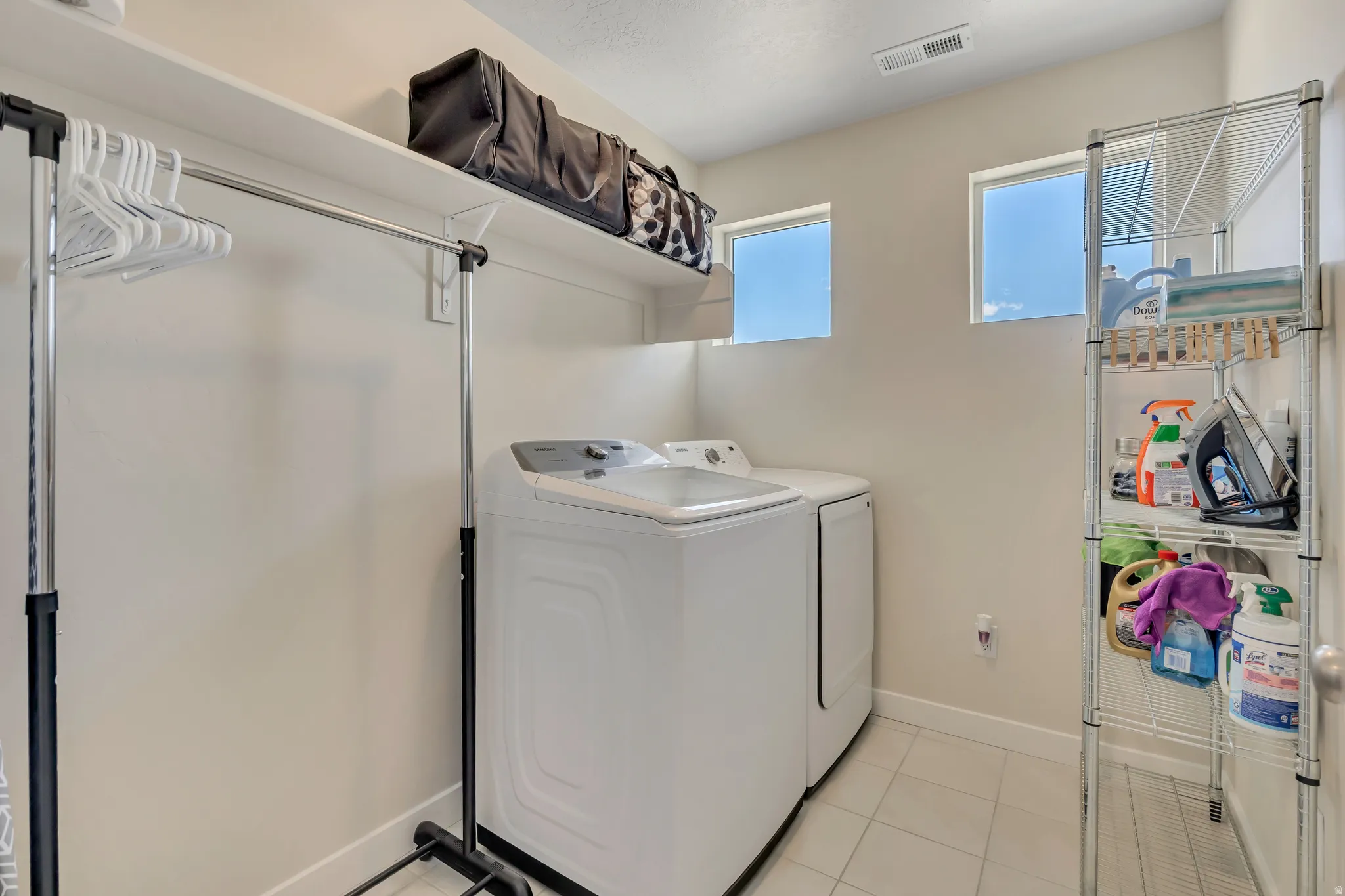 Laundry area featuring white tile flooring, upper shelving, and two windows providing natural light