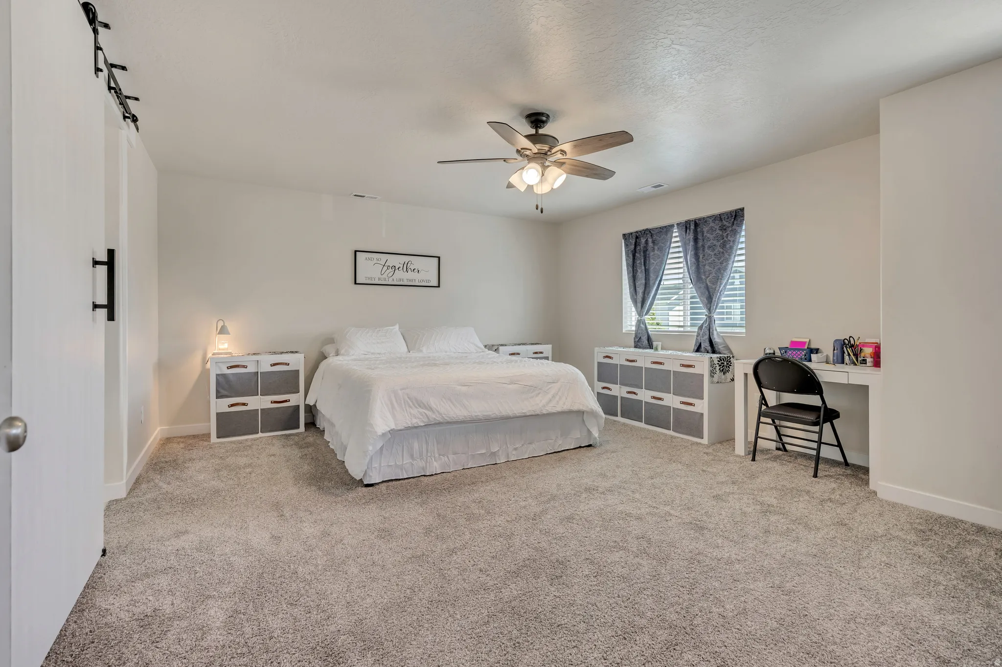 Spacious bedroom featuring plush gray carpeting, a multi-speed ceiling fan with integrated lighting, and white walls