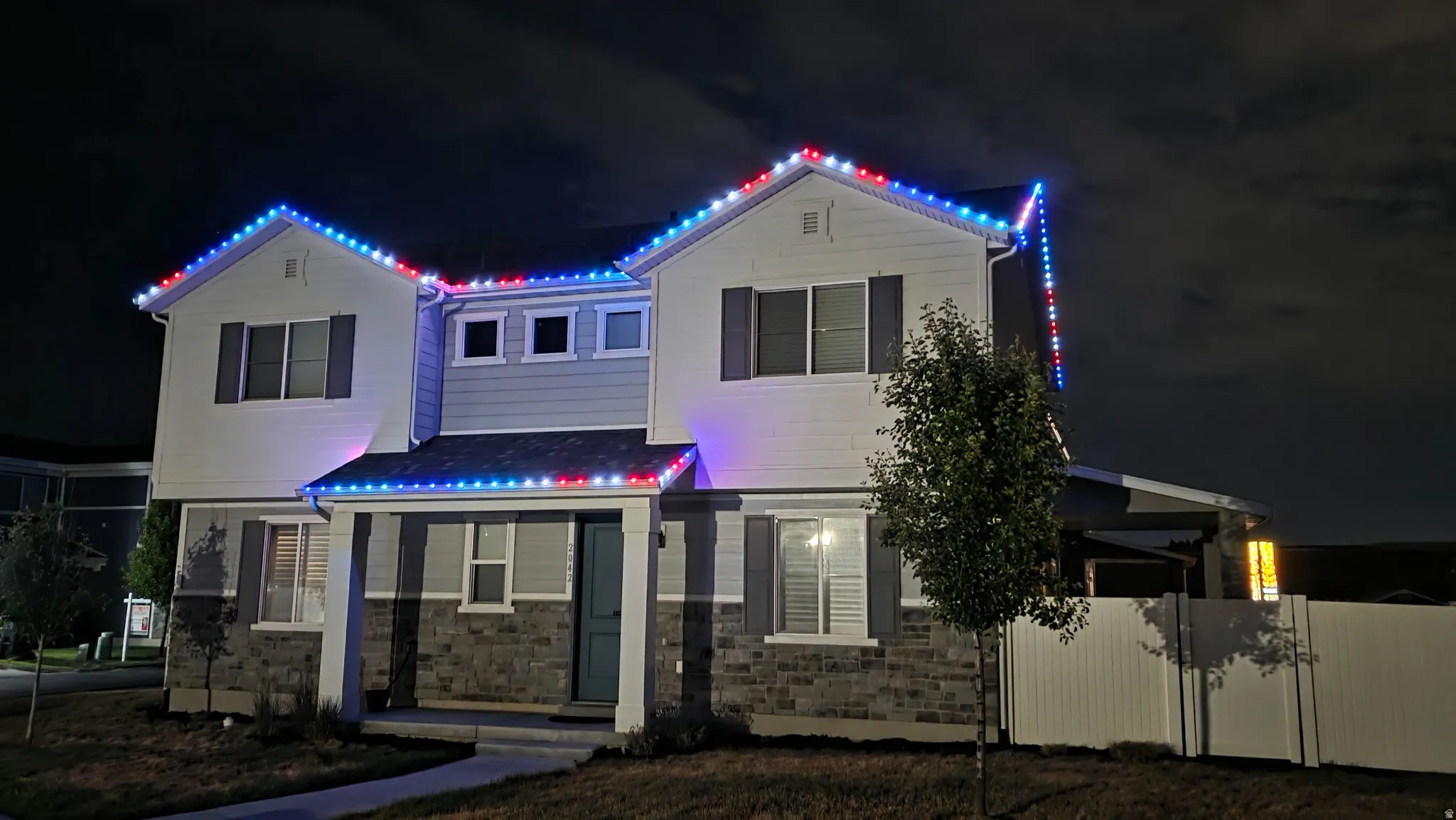 Two-story residence featuring a combination of light and dark siding, stone veneer accents, and a covered entry - permanent exterior custom holiday lighting