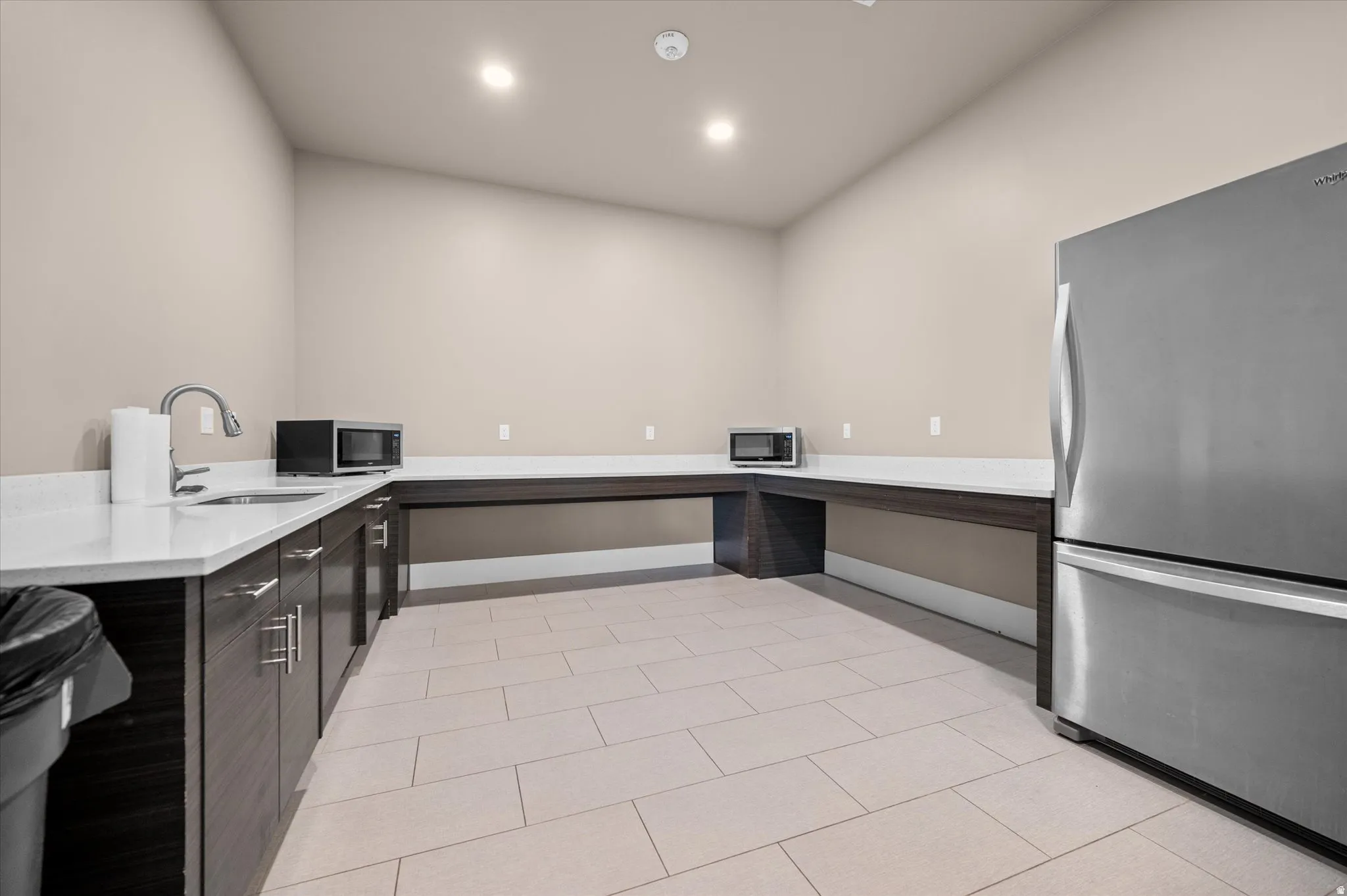 Spacious utility club house area featuring dark wood-finish cabinetry, light-toned countertops, and a stainless steel refrigerator