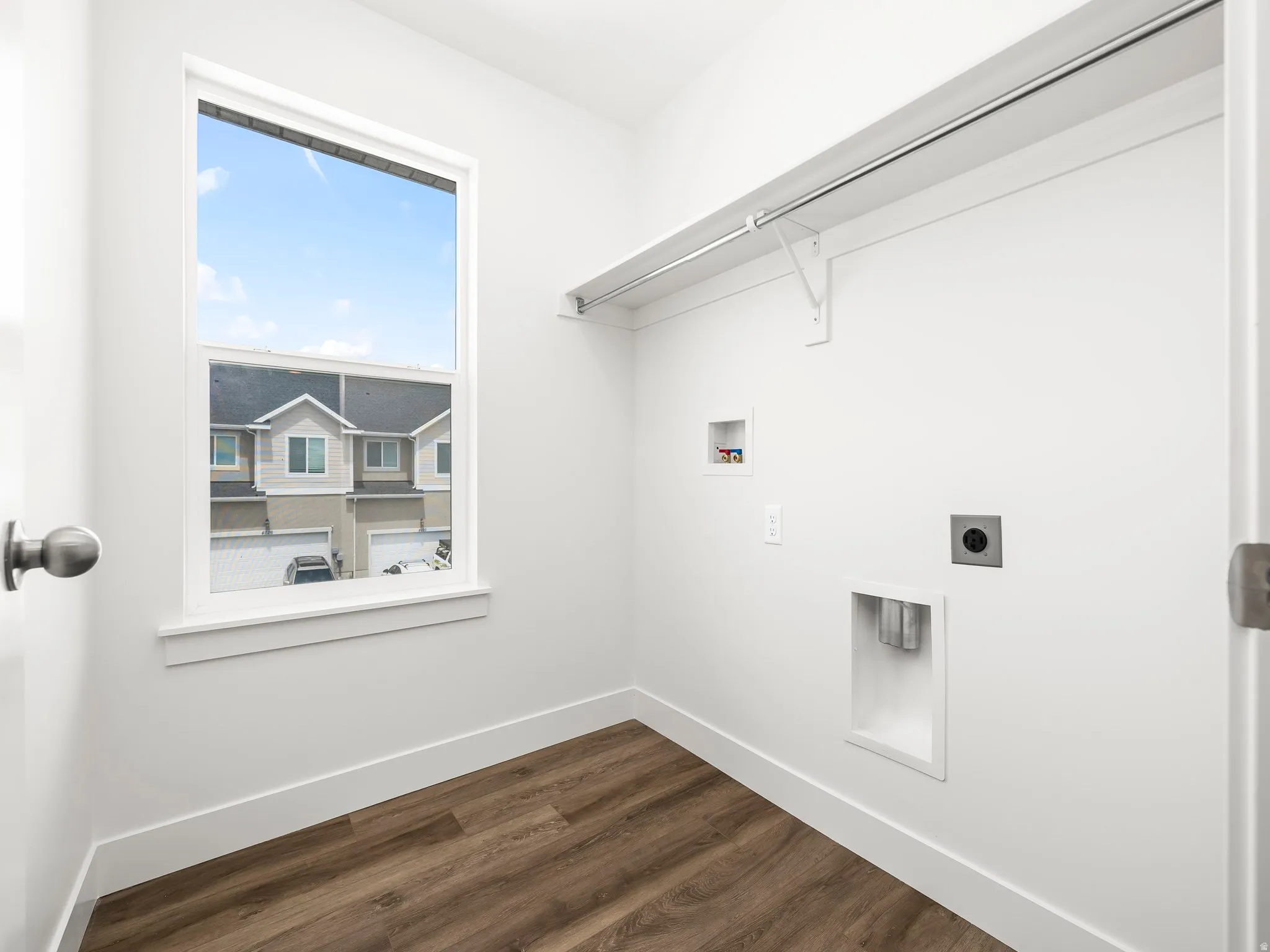 Dedicated laundry space featuring a single-pane window, wood-finish flooring, white baseboards, and a built-in hanging rod