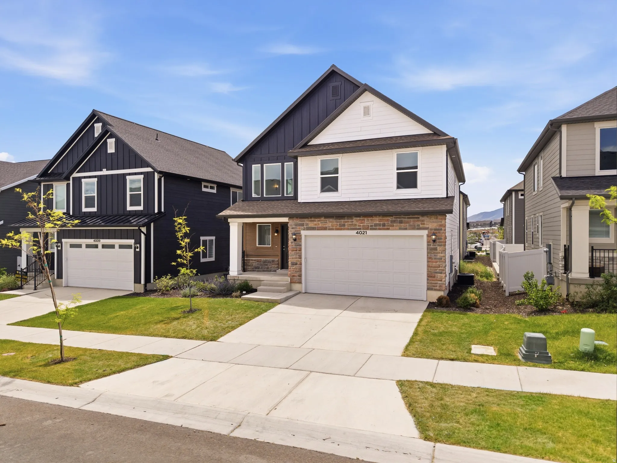 Contemporary two-story residence featuring a dark blue facade with white trim, a stone veneer accent, and a light-colored garage door