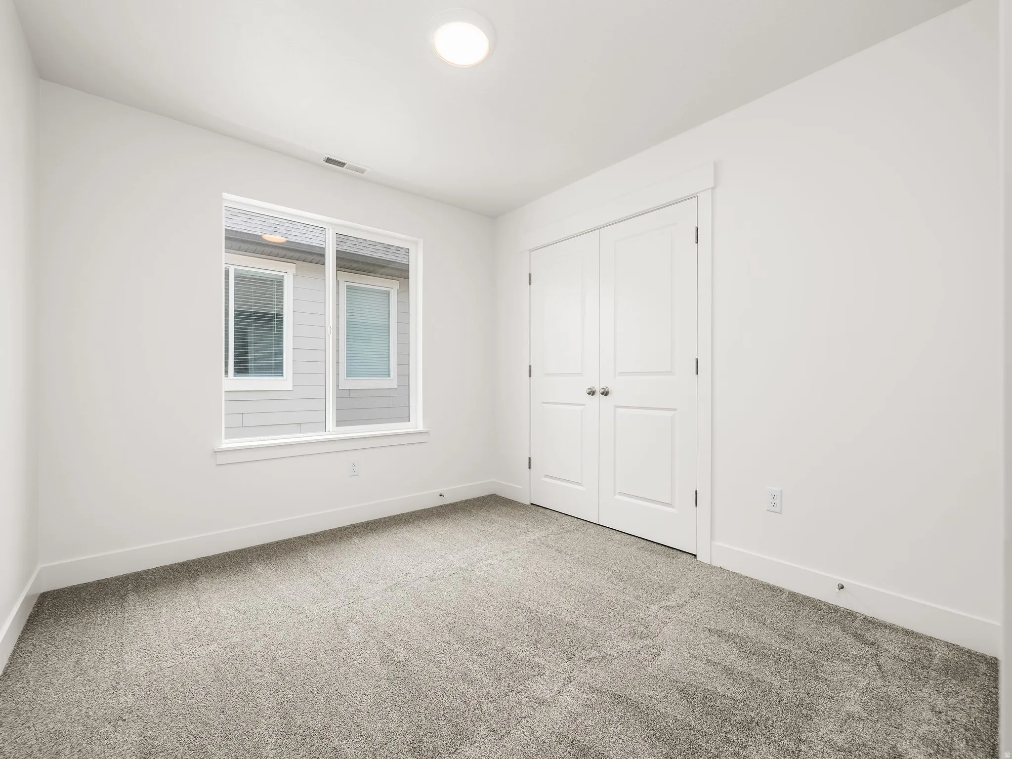 Light-filled room featuring a large window, neutral wall paint, and gray textured carpeting
