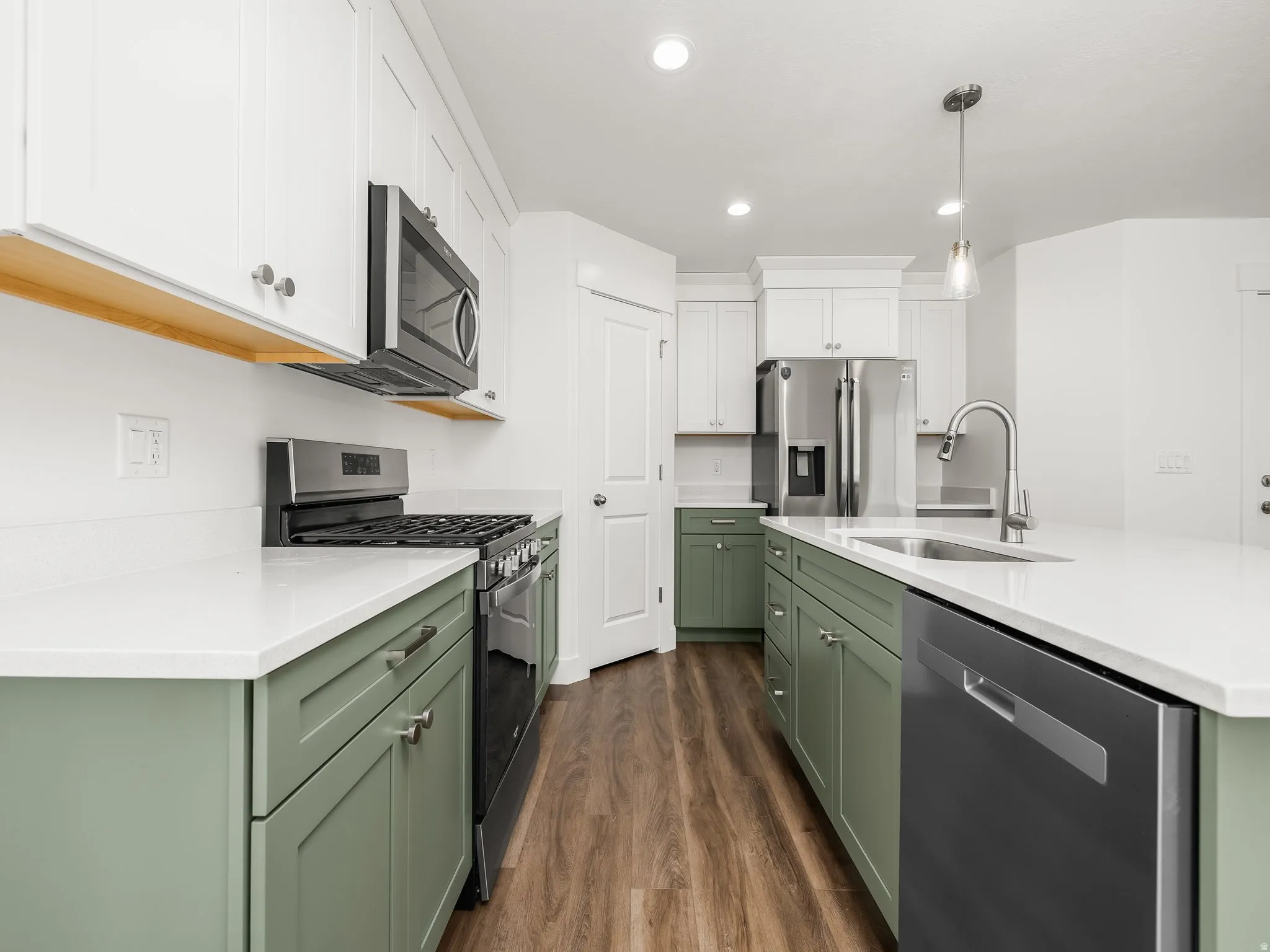 Modern kitchen featuring two-tone cabinetry with white upper cabinets and sage green lower cabinets, stainless steel appliances, white countertops, and wood-finish flooring