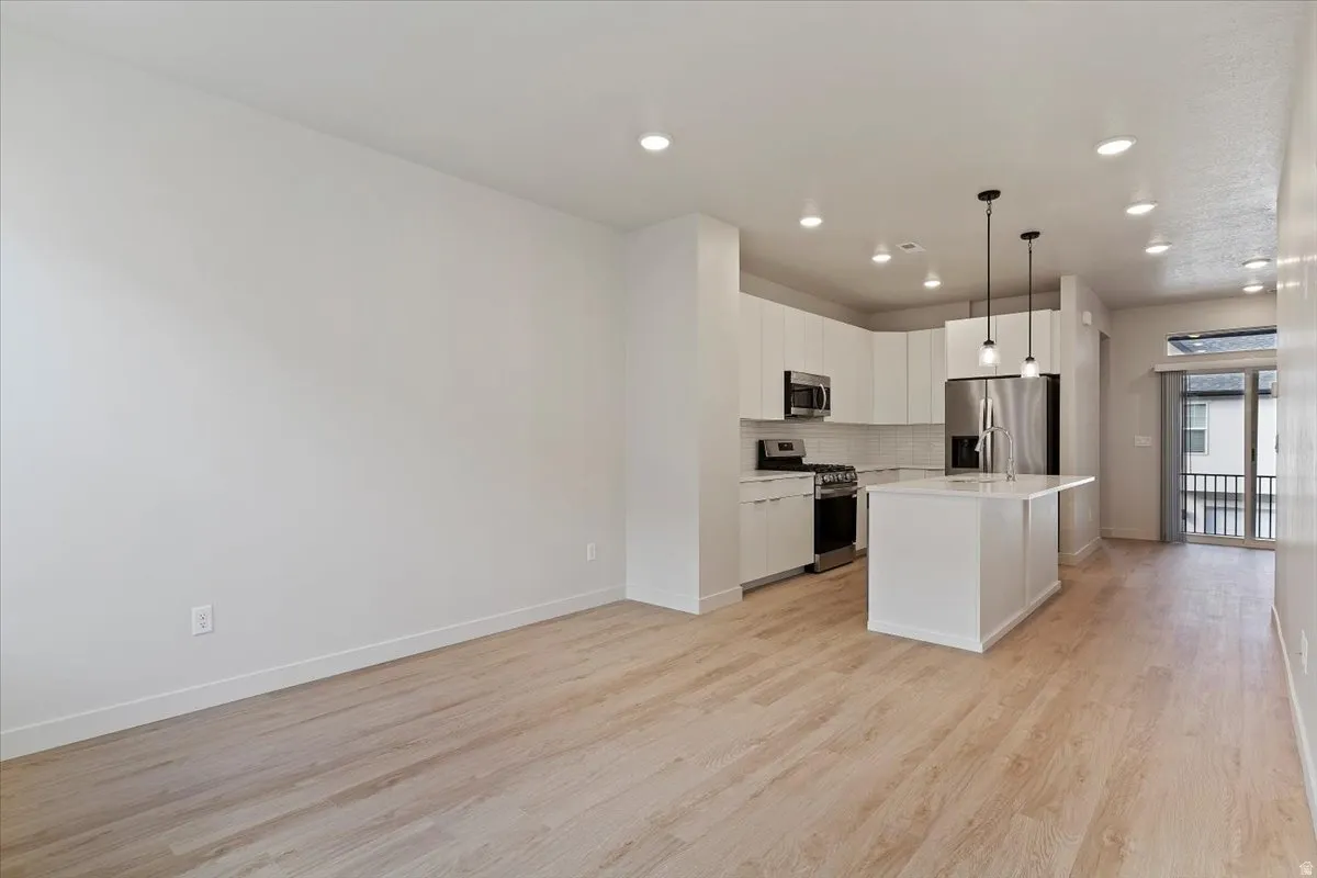 Contemporary kitchen featuring a white island, stainless steel appliances, white cabinetry, and wood-finish flooring