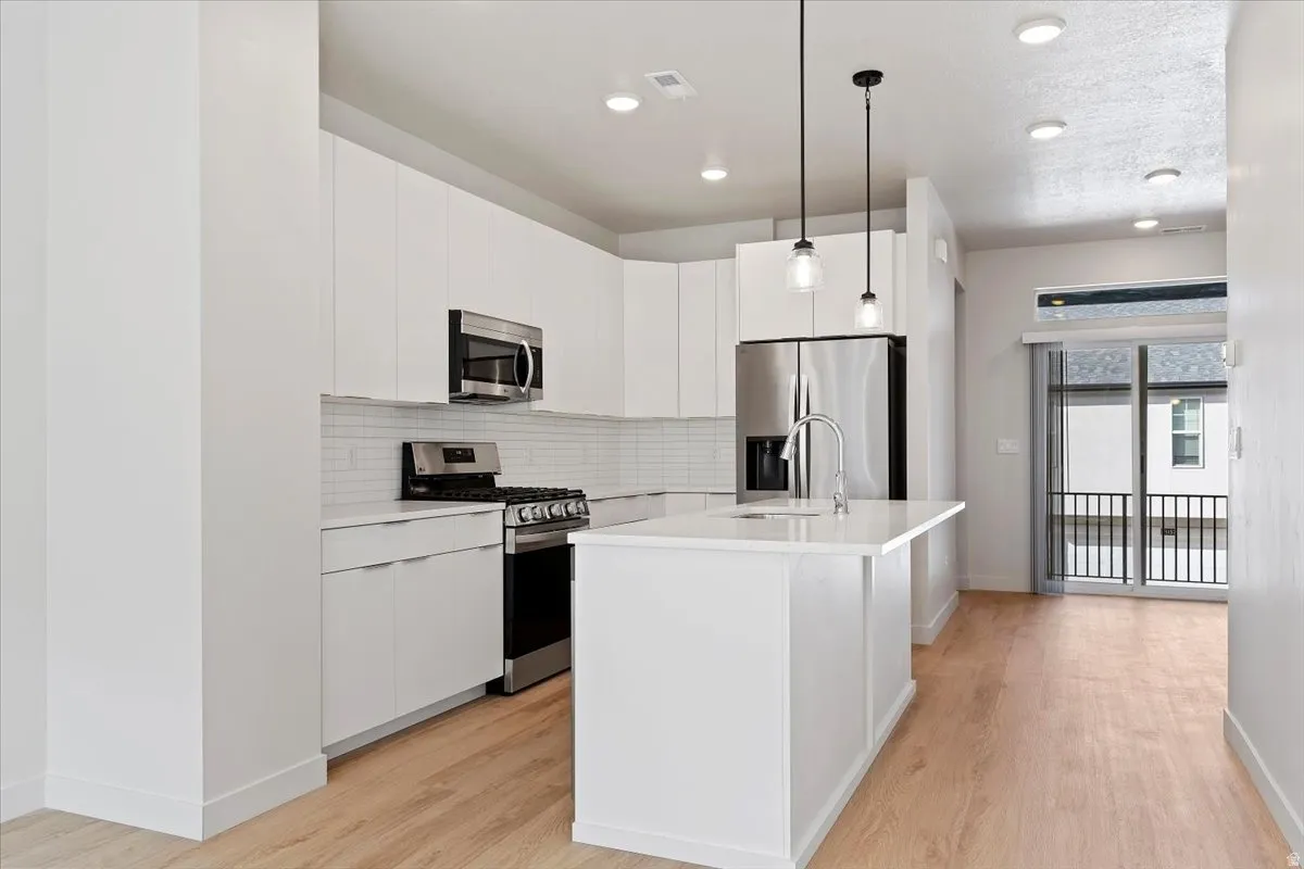 Contemporary kitchen featuring white cabinetry, stainless steel appliances, white subway tile backsplash, and a central island with dual pendant lighting