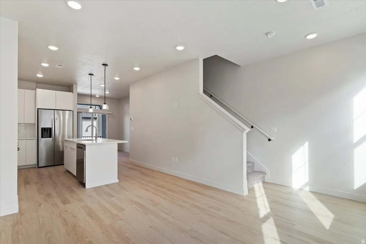 Open-concept living space featuring wood-finish flooring, a contemporary kitchen island with pendant lighting, white cabinetry, stainless steel appliances, and recessed ceiling lighting