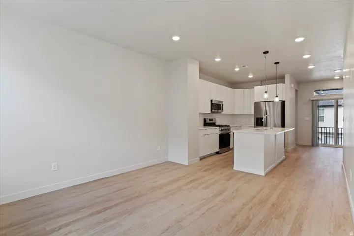 Contemporary kitchen featuring a white island, stainless steel appliances, white cabinetry, and wood-finish flooring