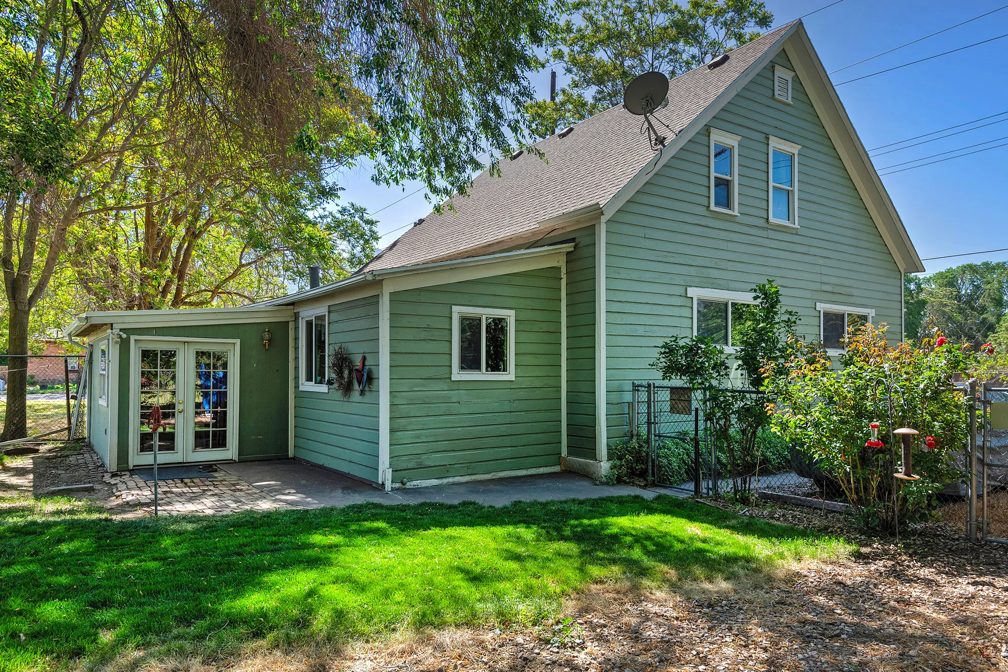 Green siding exterior featuring a pitched roof, multiple window placements, and a rear patio