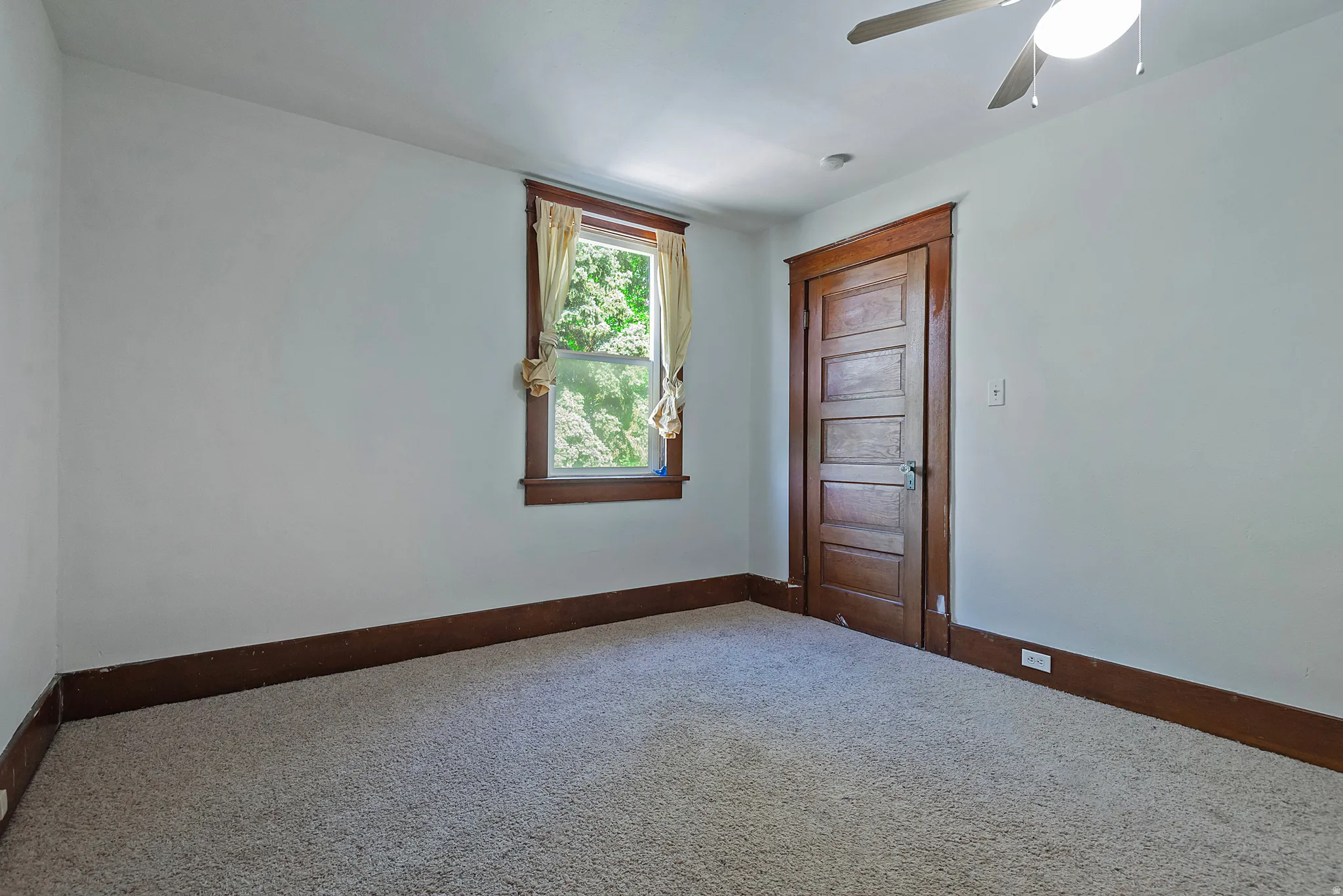 Carpeted room featuring a ceiling fan with light, a window with wood trim, and a paneled wood door with matching trim and baseboards