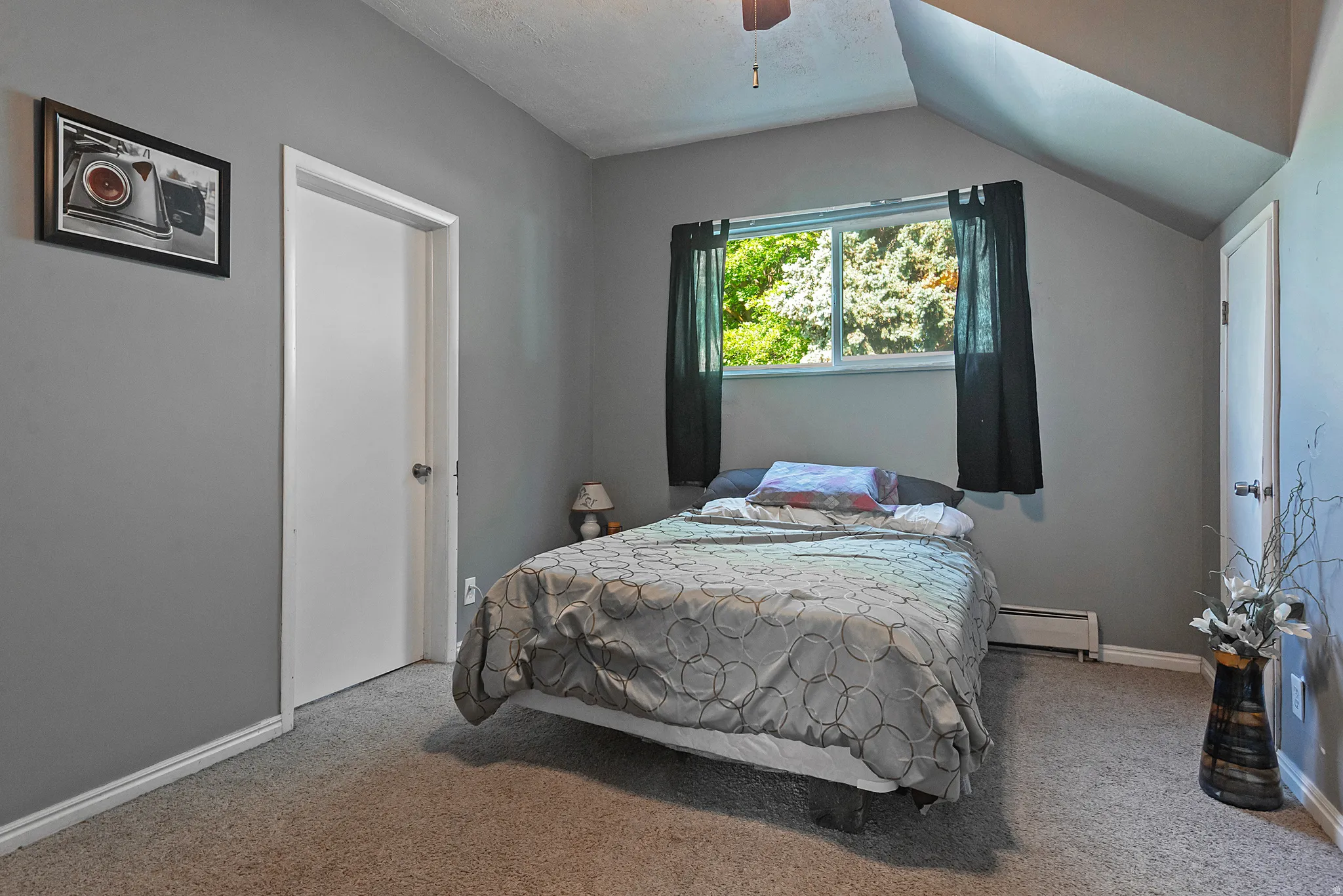 Carpeted room featuring a window with exterior tree scenery, sloped ceiling, and ceiling fan