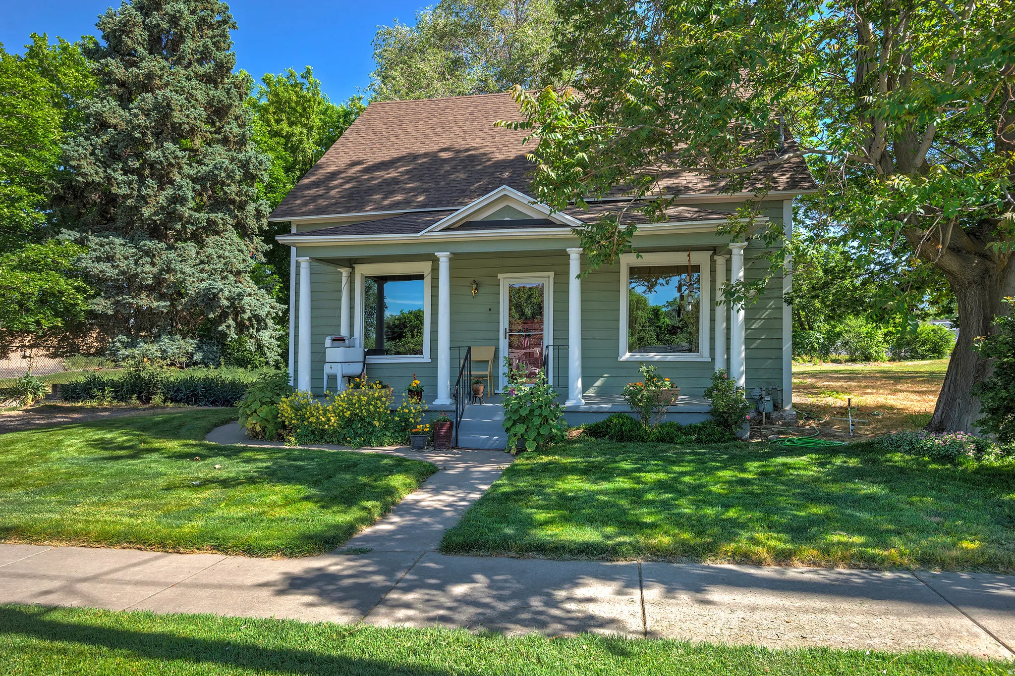 Charming single-story home featuring a covered front porch with white columns, a pitched roof, and light green siding