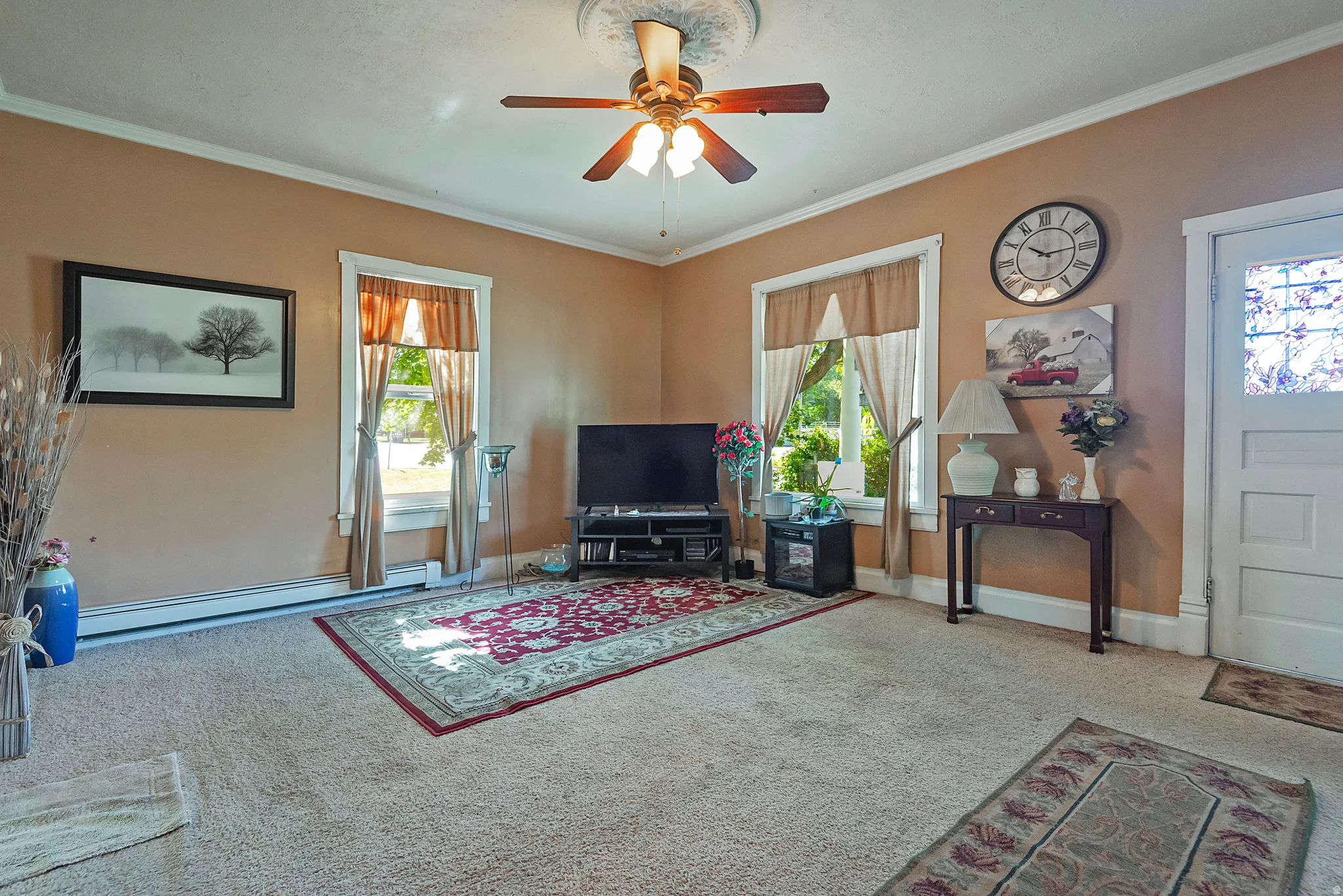 Interior living space featuring light-colored carpet, a ceiling fan with light fixture, and crown molding