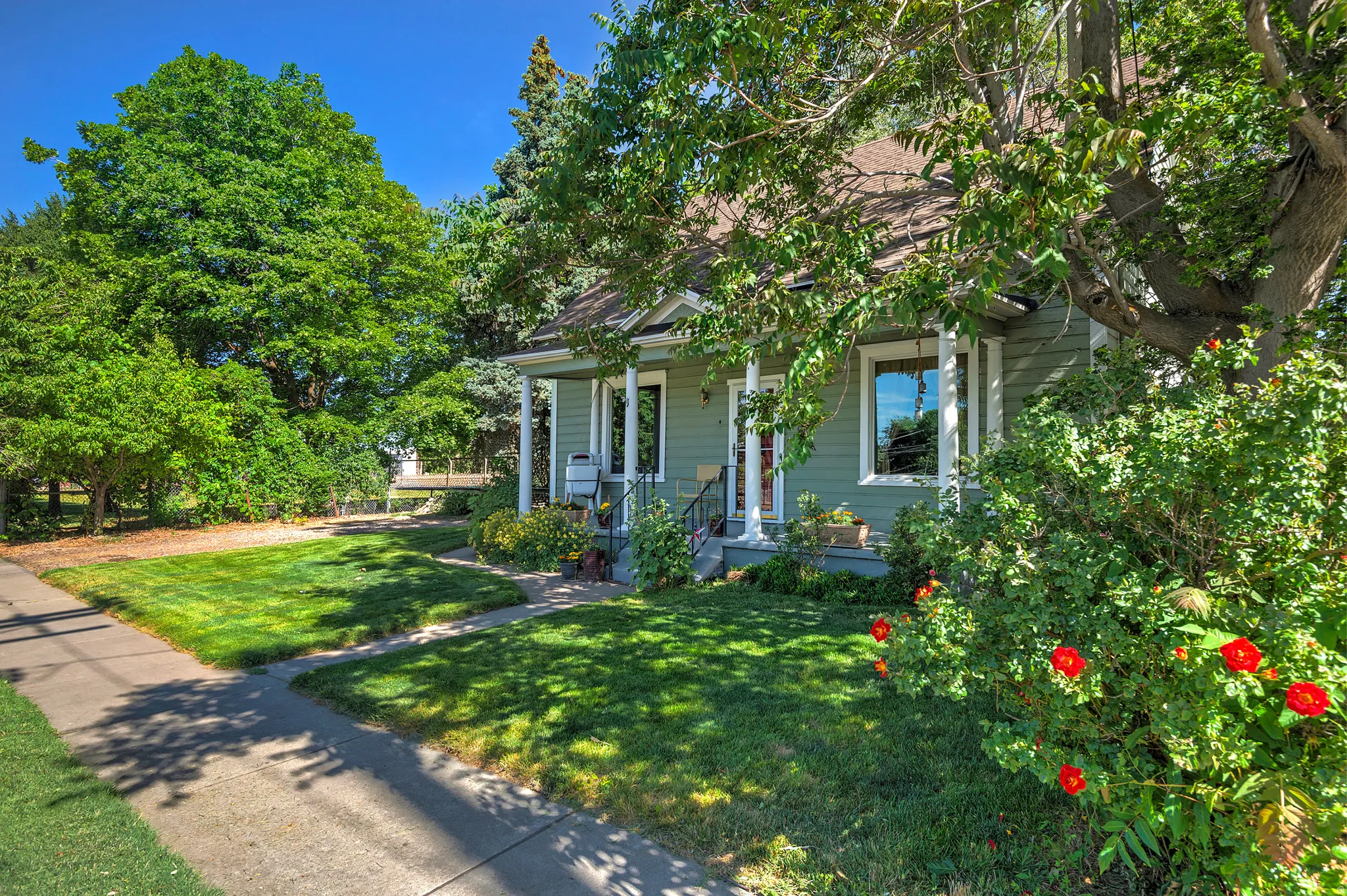 Charming single-story residence featuring a covered front porch with white columns, light green siding, and a gabled roof