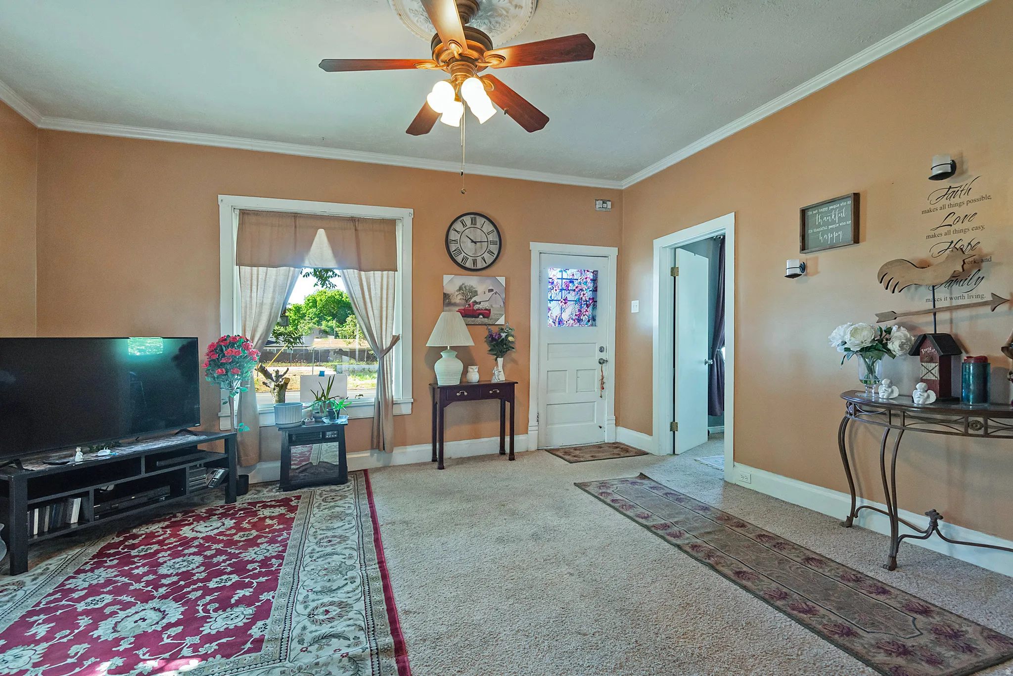 Carpeted living area featuring a ceiling fan with light fixture, crown molding, and two windows with natural light