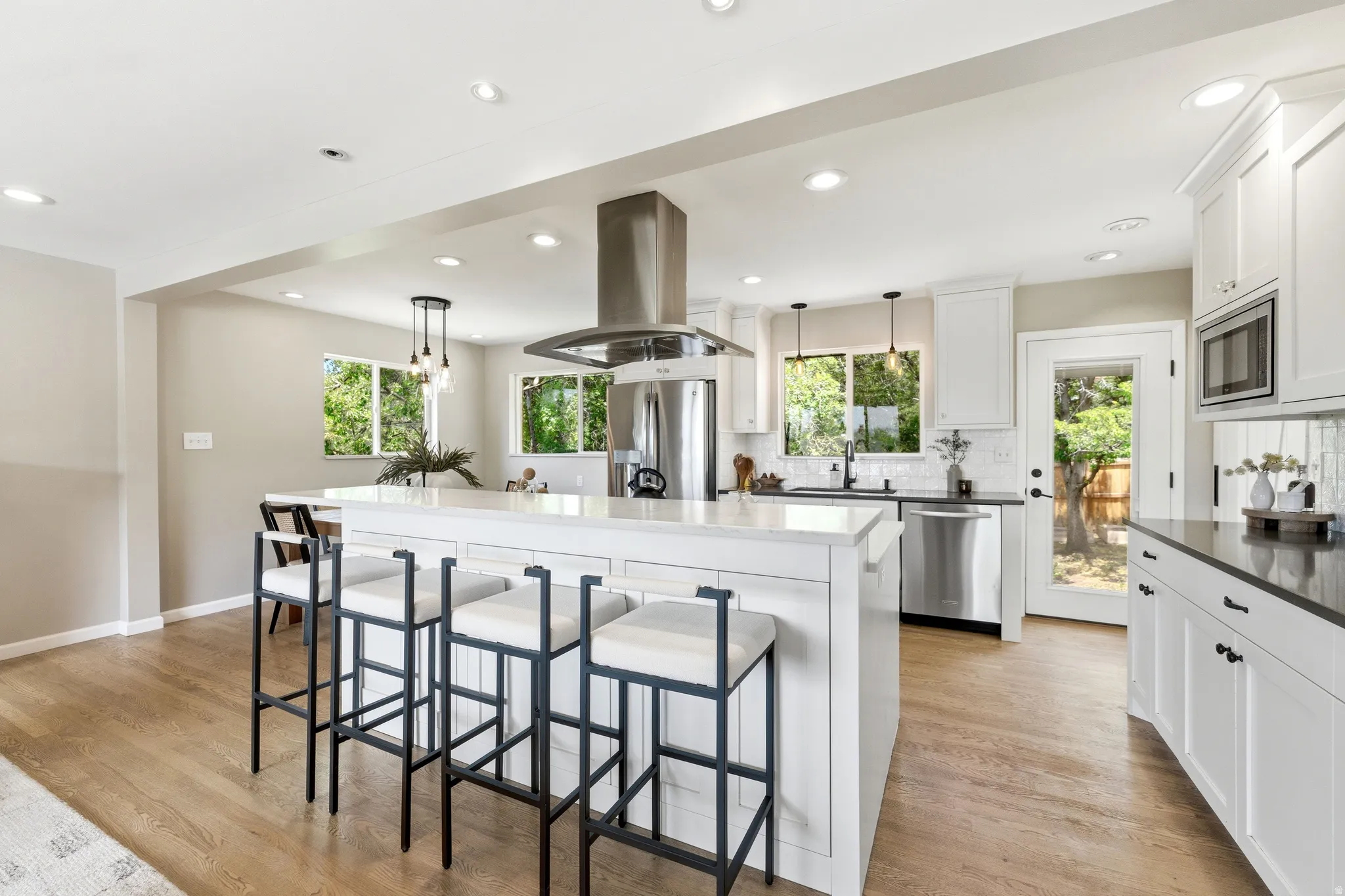 Kitchen featuring a large central island with seating, white shaker cabinetry, stainless steel appliances, and wood-finish flooring