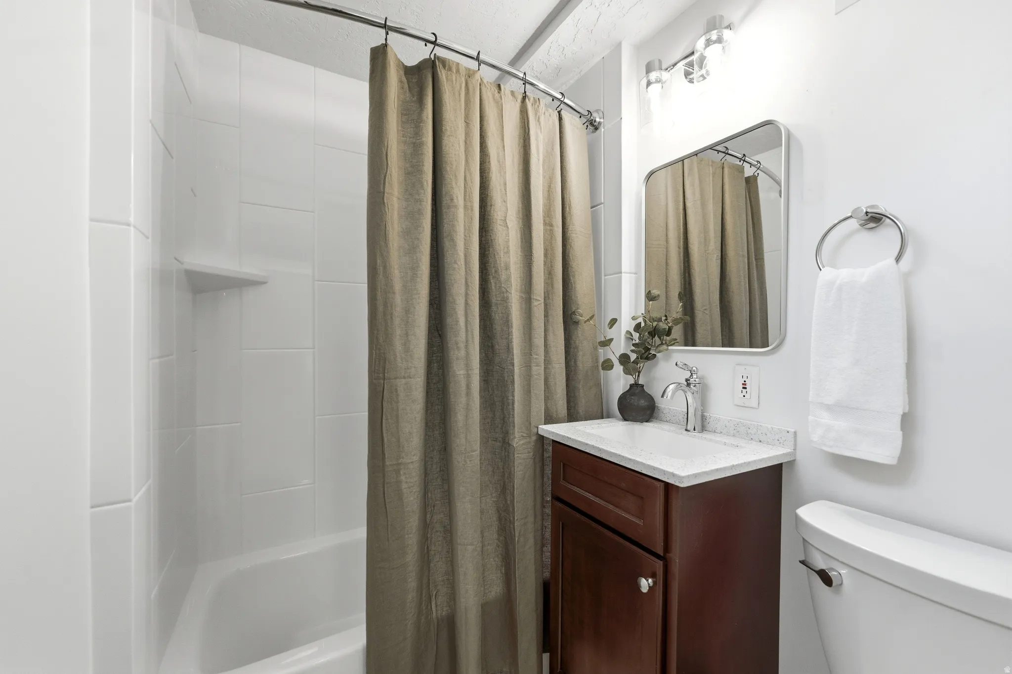 Full bathroom featuring a white tile shower surround, a white bathtub, a dark wood-finish vanity with a white countertop, a rectangular mirror, and a chrome light fixture