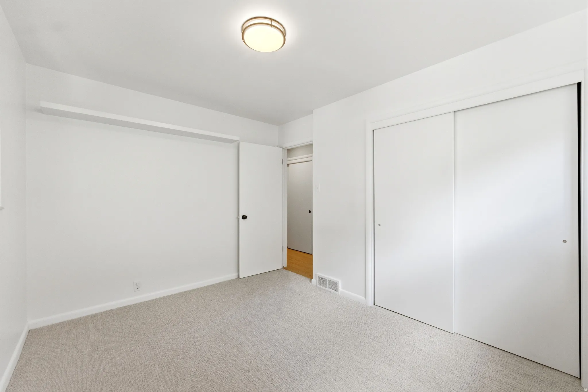 Carpeted room with white walls, a flush-mount ceiling light fixture, and a built-in closet with sliding doors
