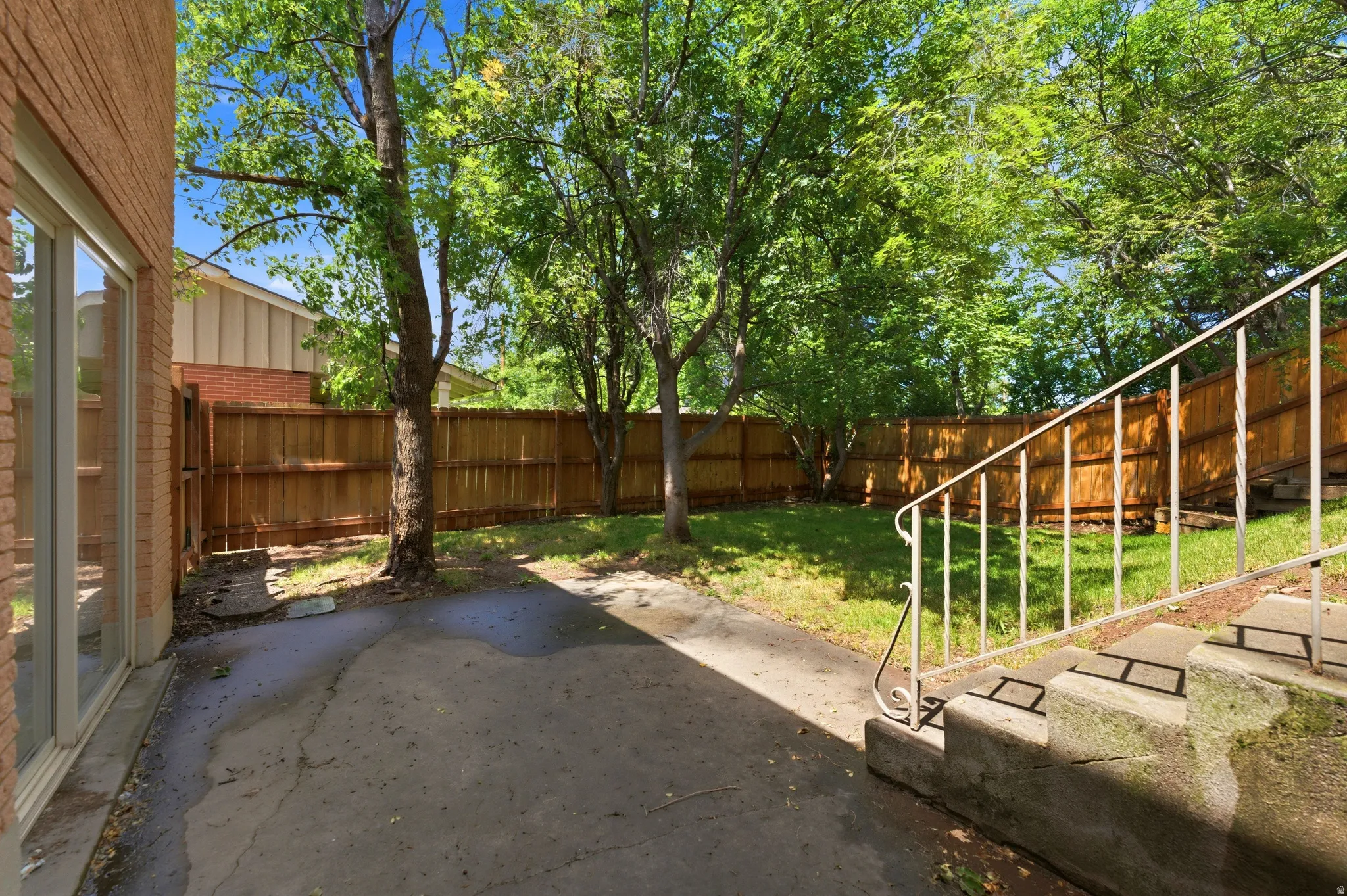 Spacious backyard featuring a privacy fence, mature trees, concrete patio space, and a grass area