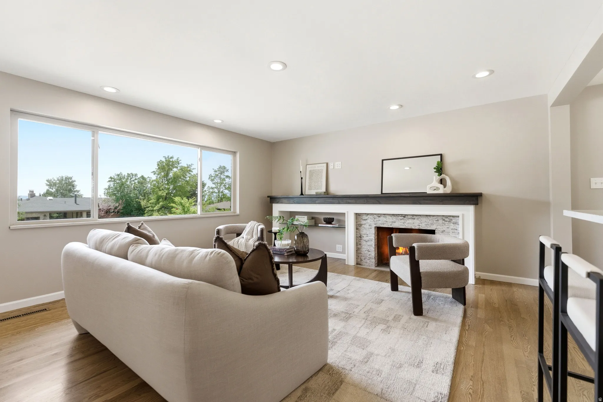 Spacious living room featuring wood-finish flooring, recessed lighting, and a stacked stone fireplace with a dark wood mantel