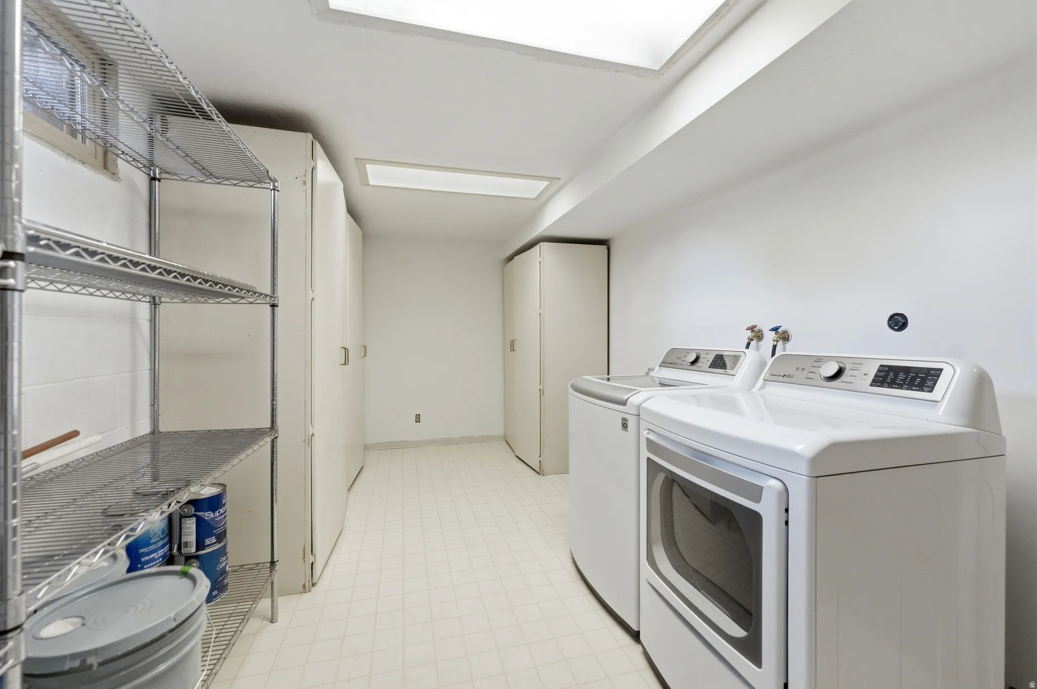Dedicated laundry area featuring white appliances, ample built-in storage cabinetry, resilient flooring, and overhead fluorescent lighting