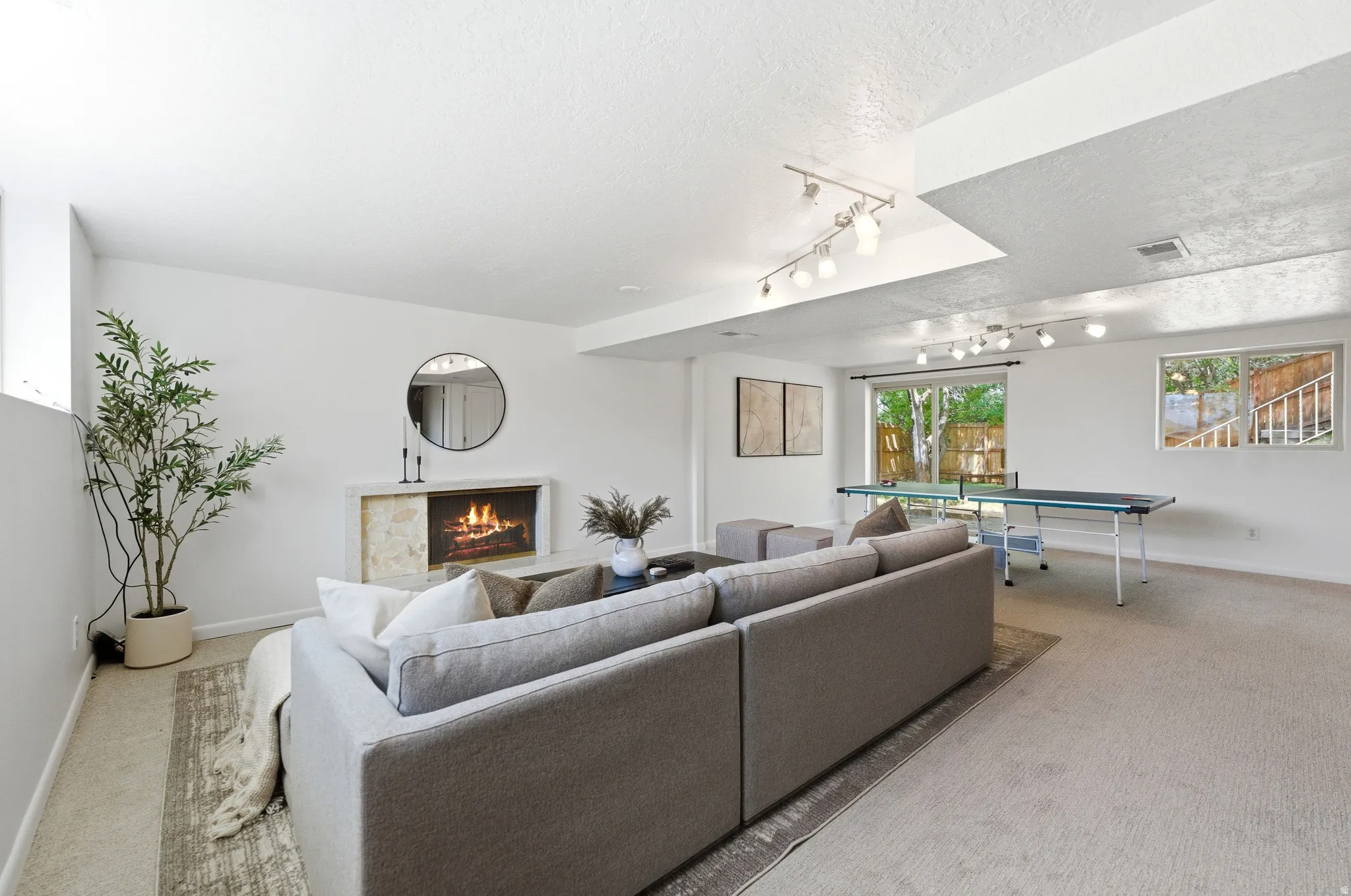 Spacious living area featuring a built-in fireplace with a stone surround, recessed lighting, track lighting, and a large window providing natural light