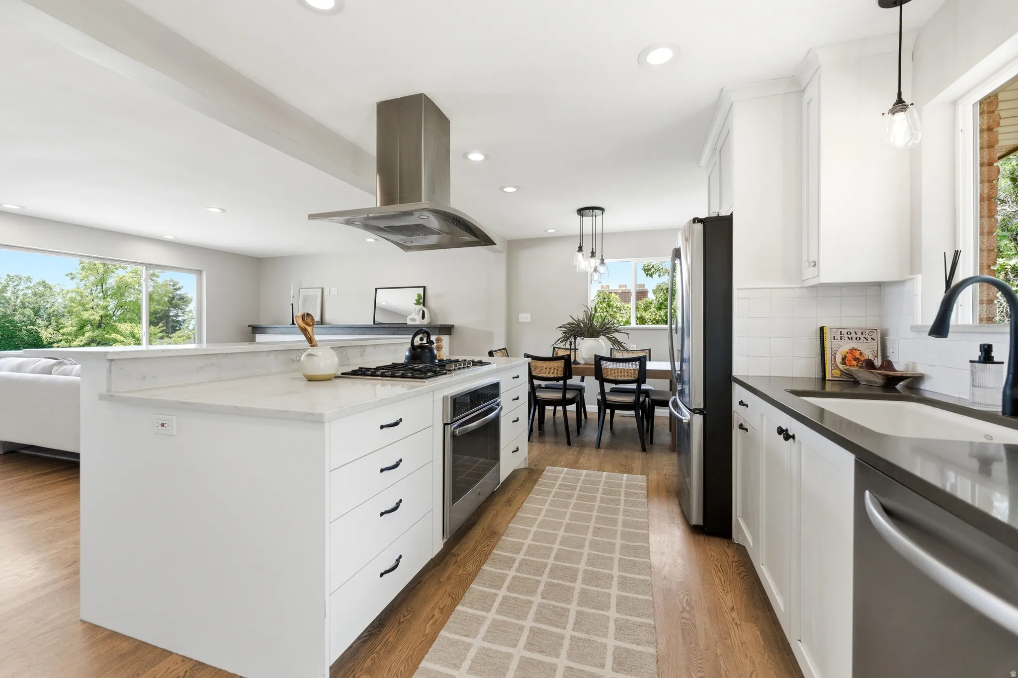 Modern kitchen featuring white cabinetry, a large center island with a built-in range, stainless steel appliances, and wood-finish flooring