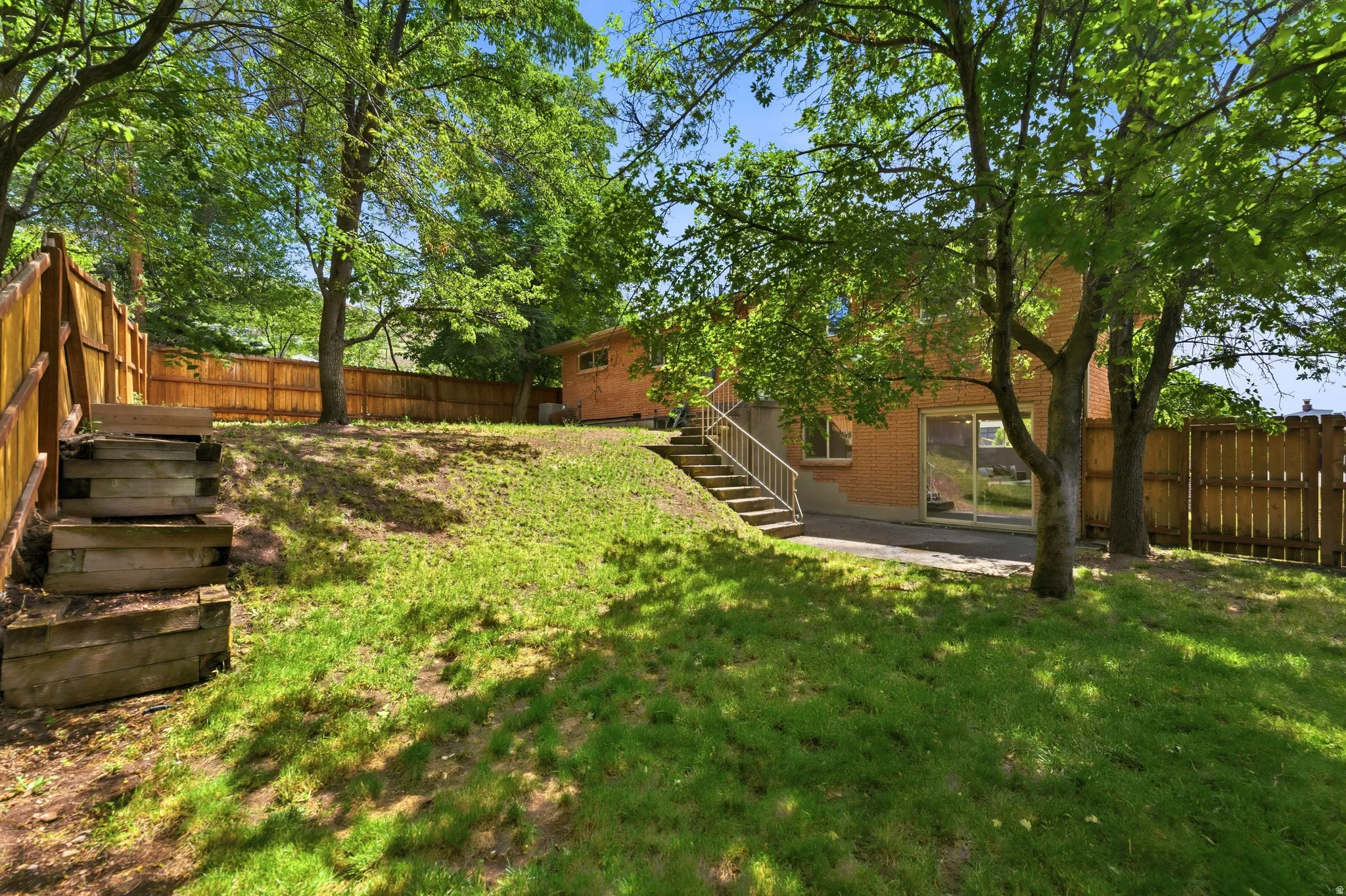Expansive terraced backyard featuring a manicured lawn, established trees, and a full privacy fence