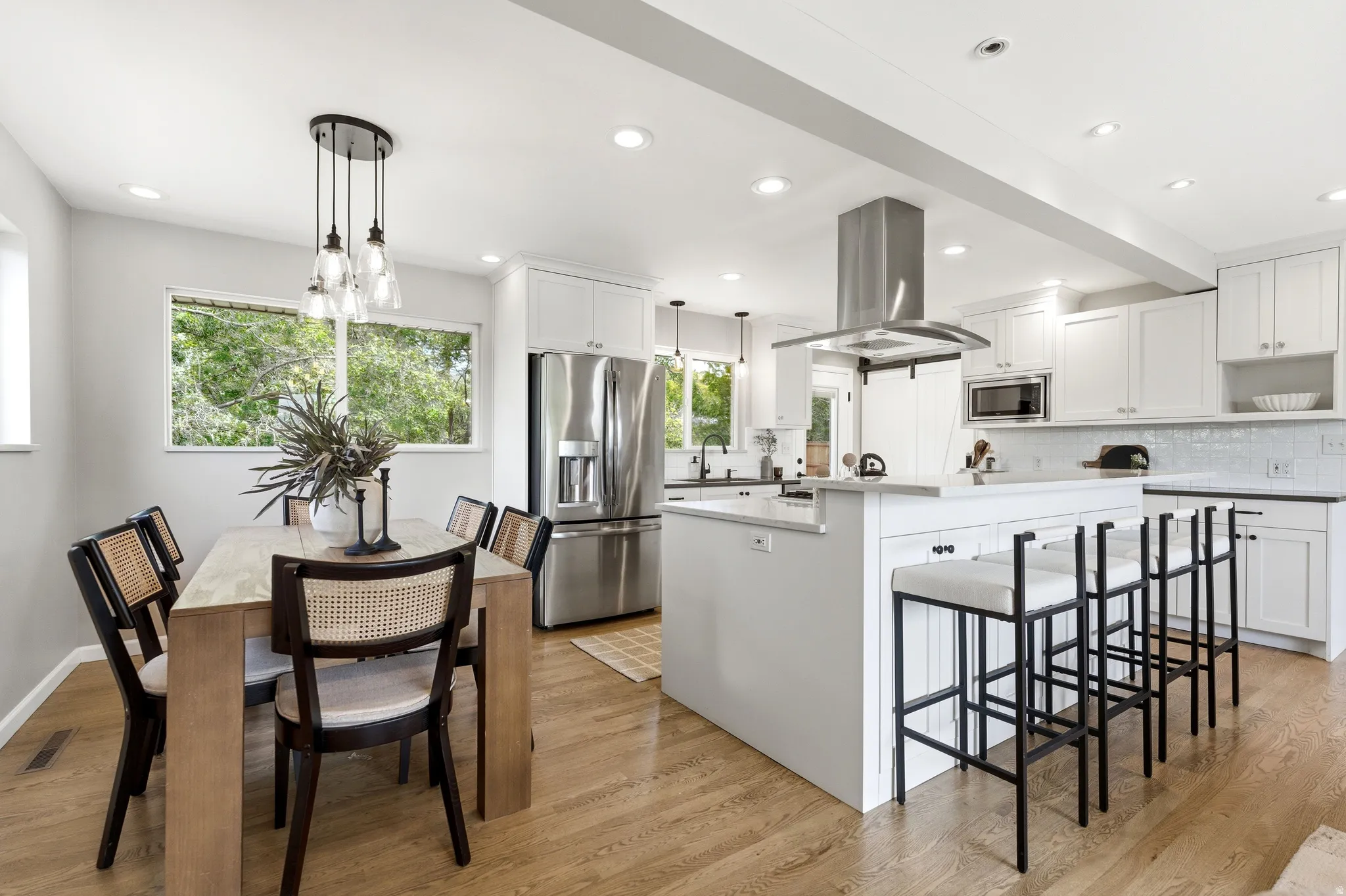 Open-concept kitchen and dining area featuring light wood-finish flooring, white cabinetry, stainless steel appliances, a center island with bar seating, and recessed lighting