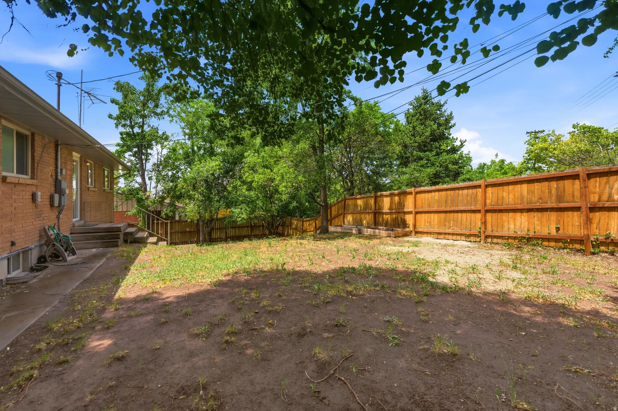 Expansive backyard featuring a new privacy fence, mature trees, a concrete patio, and exterior brick siding