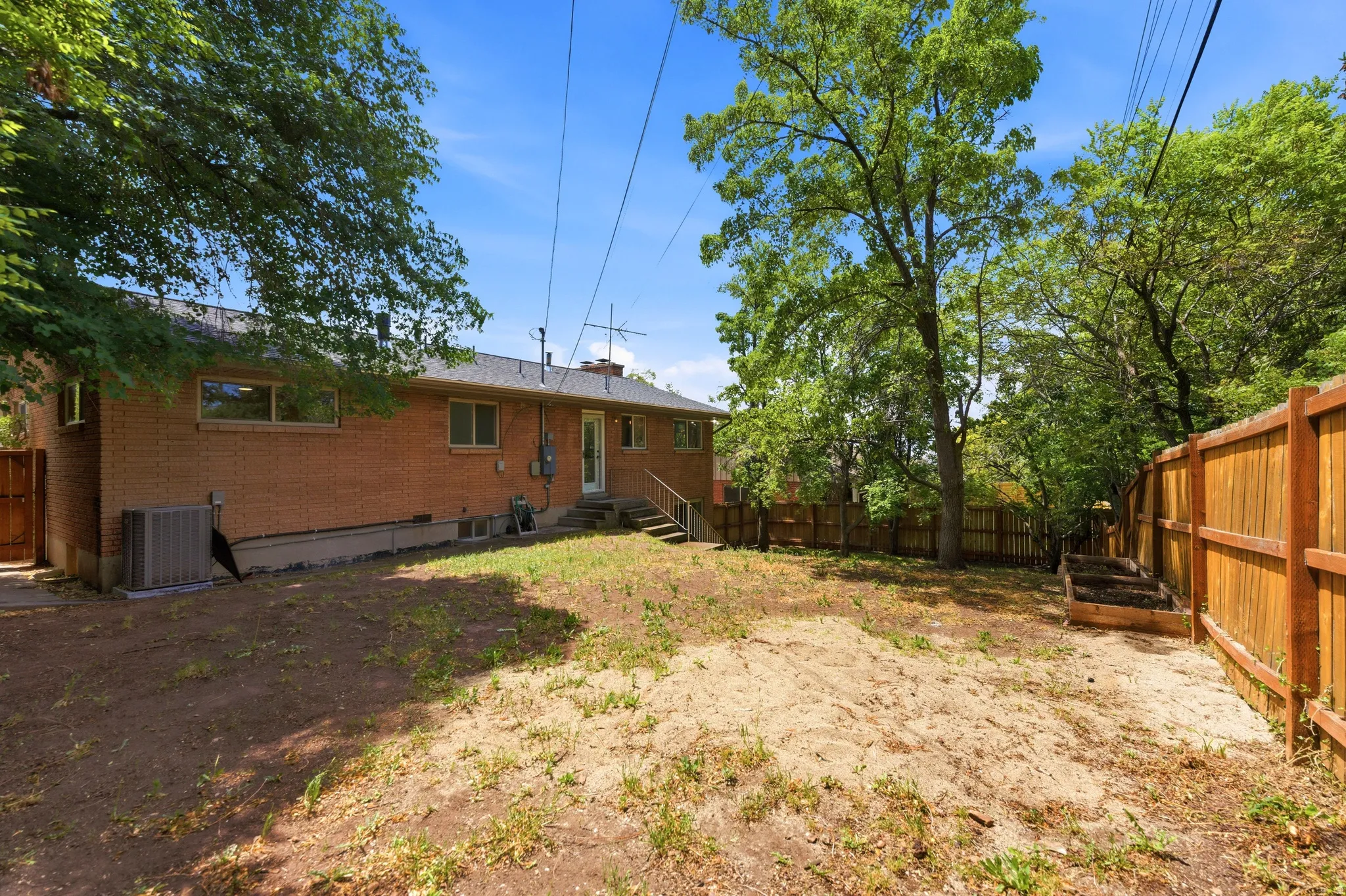 Expansive rear yard featuring a brick-clad home exterior, mature trees, and a wood fence