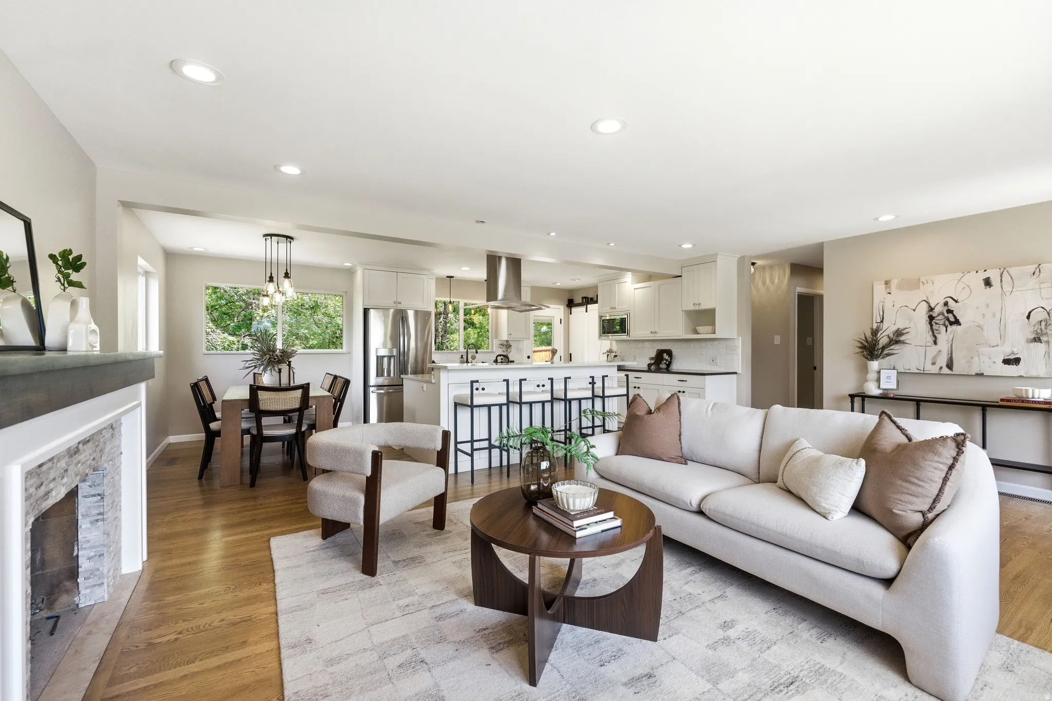 Open-concept living space featuring wood-finish flooring, recessed lighting, and a stone-clad fireplace