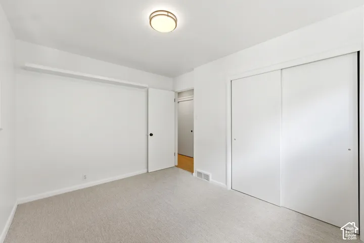 Carpeted room with white walls, a flush-mount ceiling light fixture, and a built-in closet with sliding doors