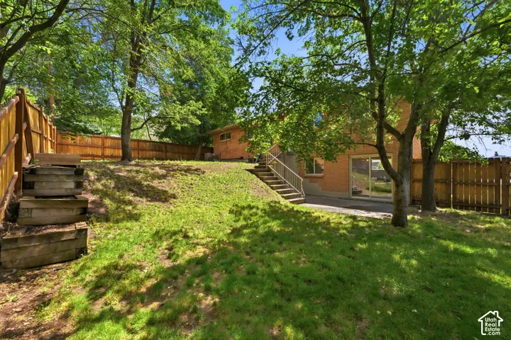 Expansive terraced backyard featuring a manicured lawn, established trees, and a full privacy fence