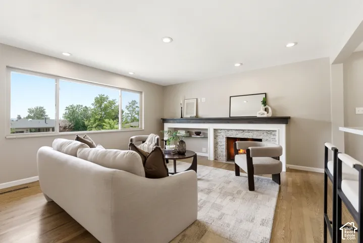 Spacious living room featuring wood-finish flooring, recessed lighting, and a stacked stone fireplace with a dark wood mantel