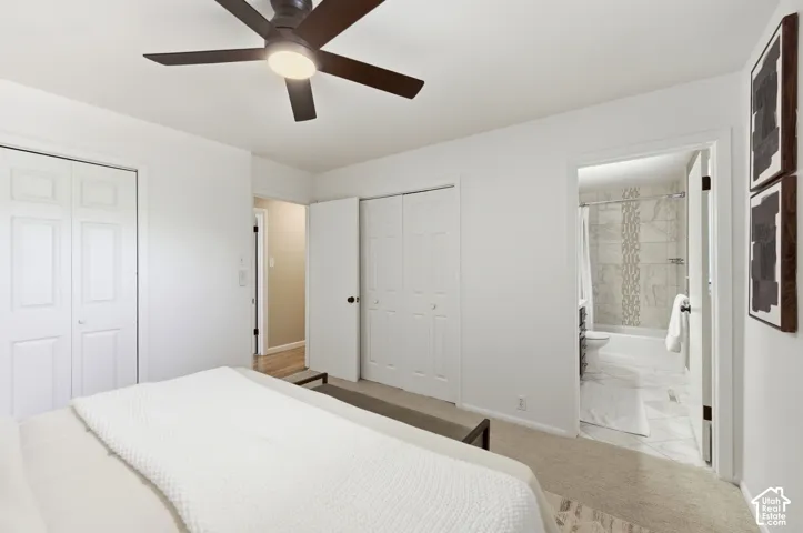 Neutral colored bedroom featuring a ceiling fan with integrated lighting, two bi-fold closet doors, and an en-suite bathroom with tiled flooring and a tiled shower surround
