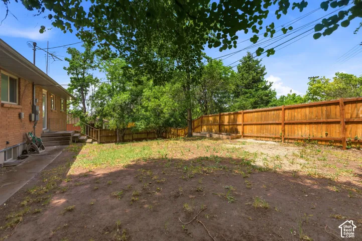Expansive backyard featuring a new privacy fence, mature trees, a concrete patio, and exterior brick siding