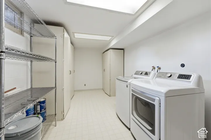 Dedicated laundry area featuring white appliances, ample built-in storage cabinetry, resilient flooring, and overhead fluorescent lighting